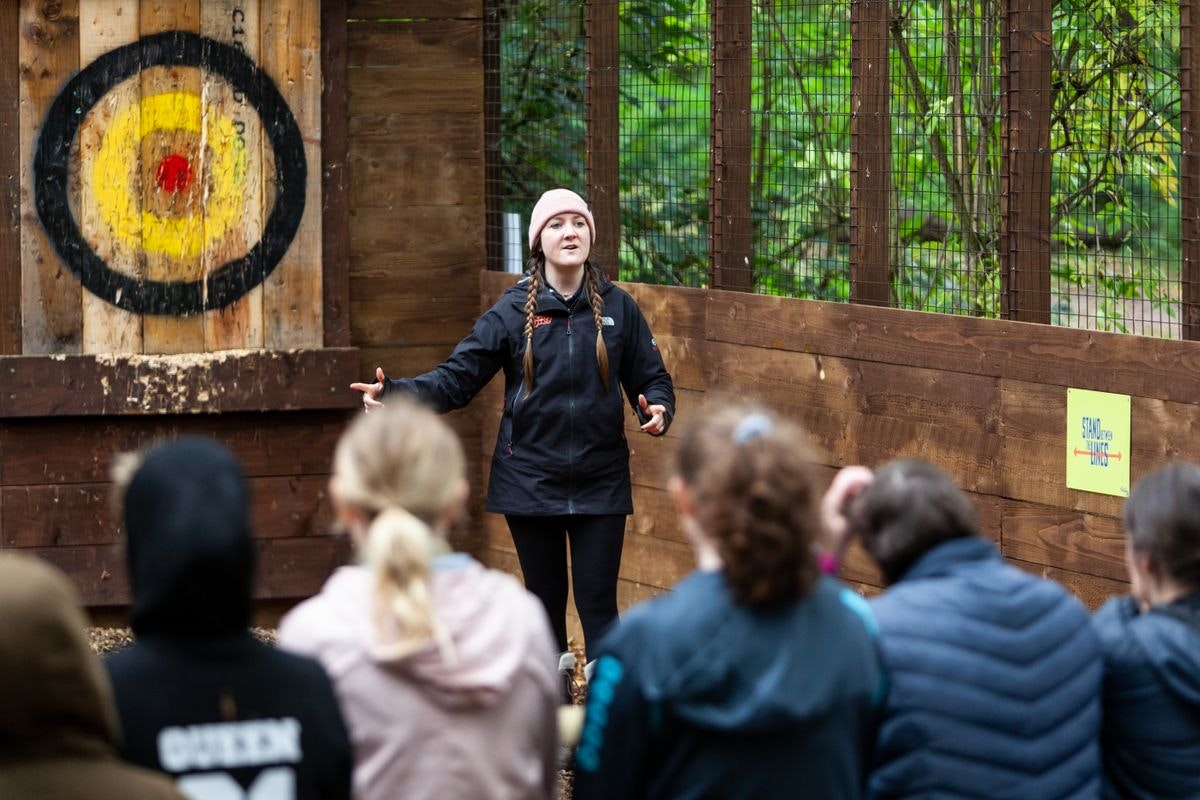 Axe throwing facilitator leads team-building event in rustic Go Ape Rivington setting.