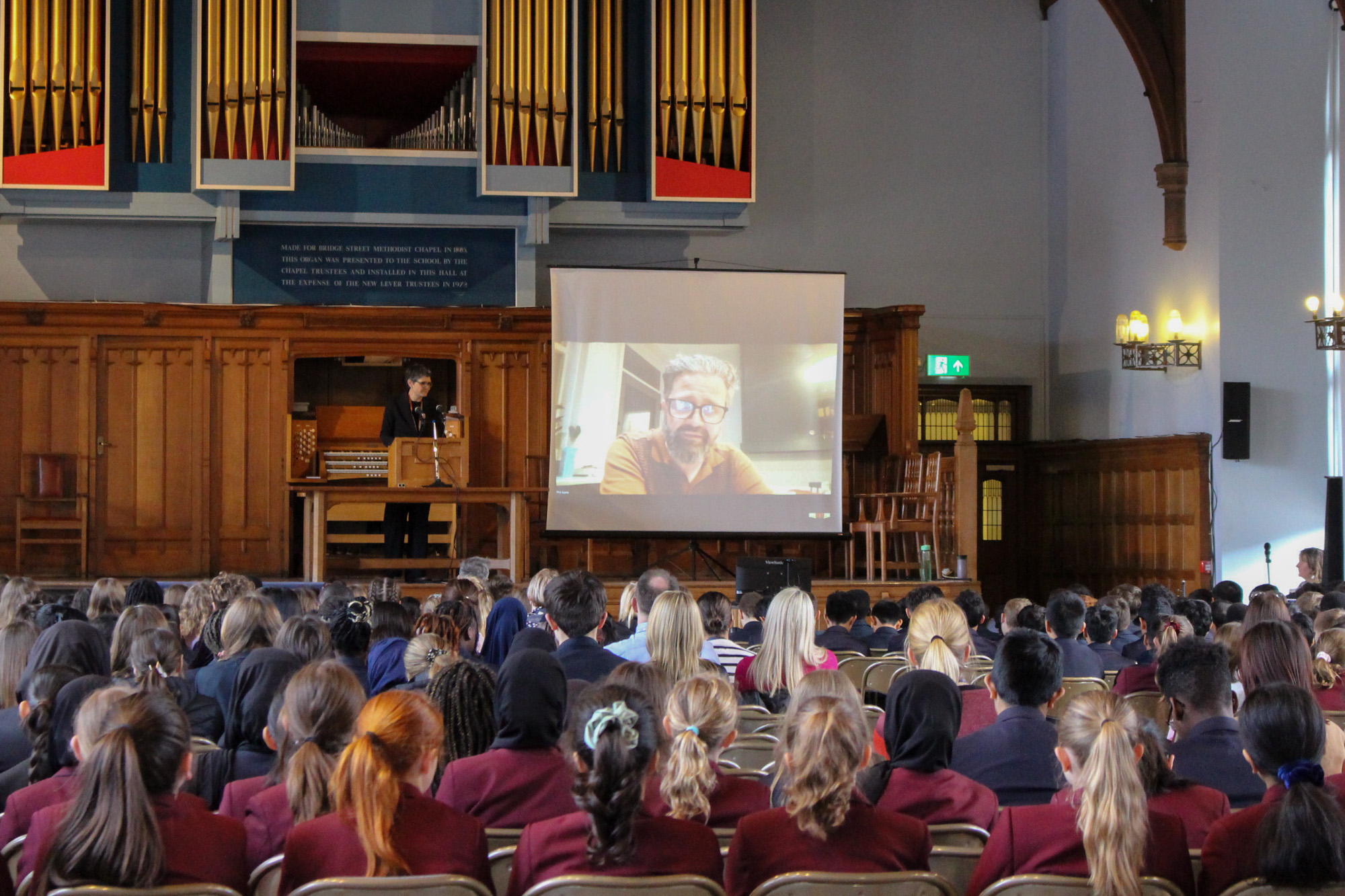 Hybrid conference room with engaged audience and historic backdrop at Bridge School.