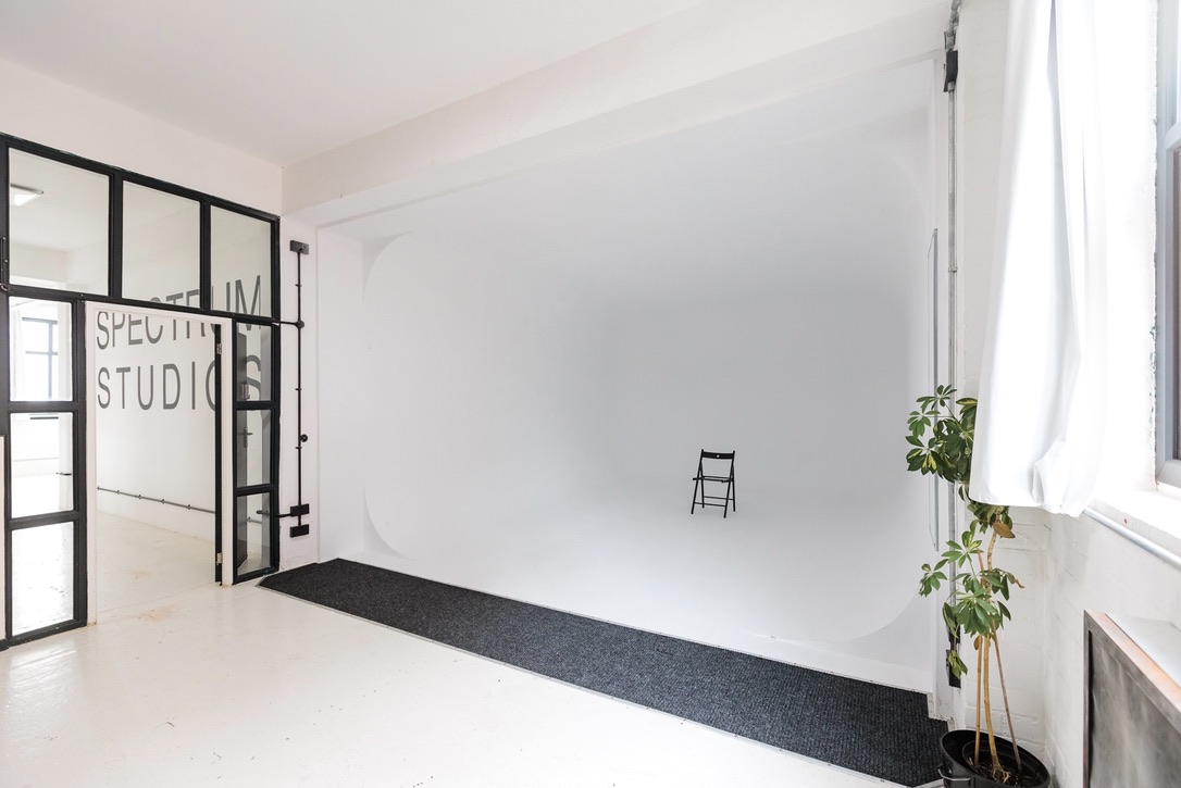 Minimalist event space with white backdrop and chair, ideal for workshops and photo shoots.