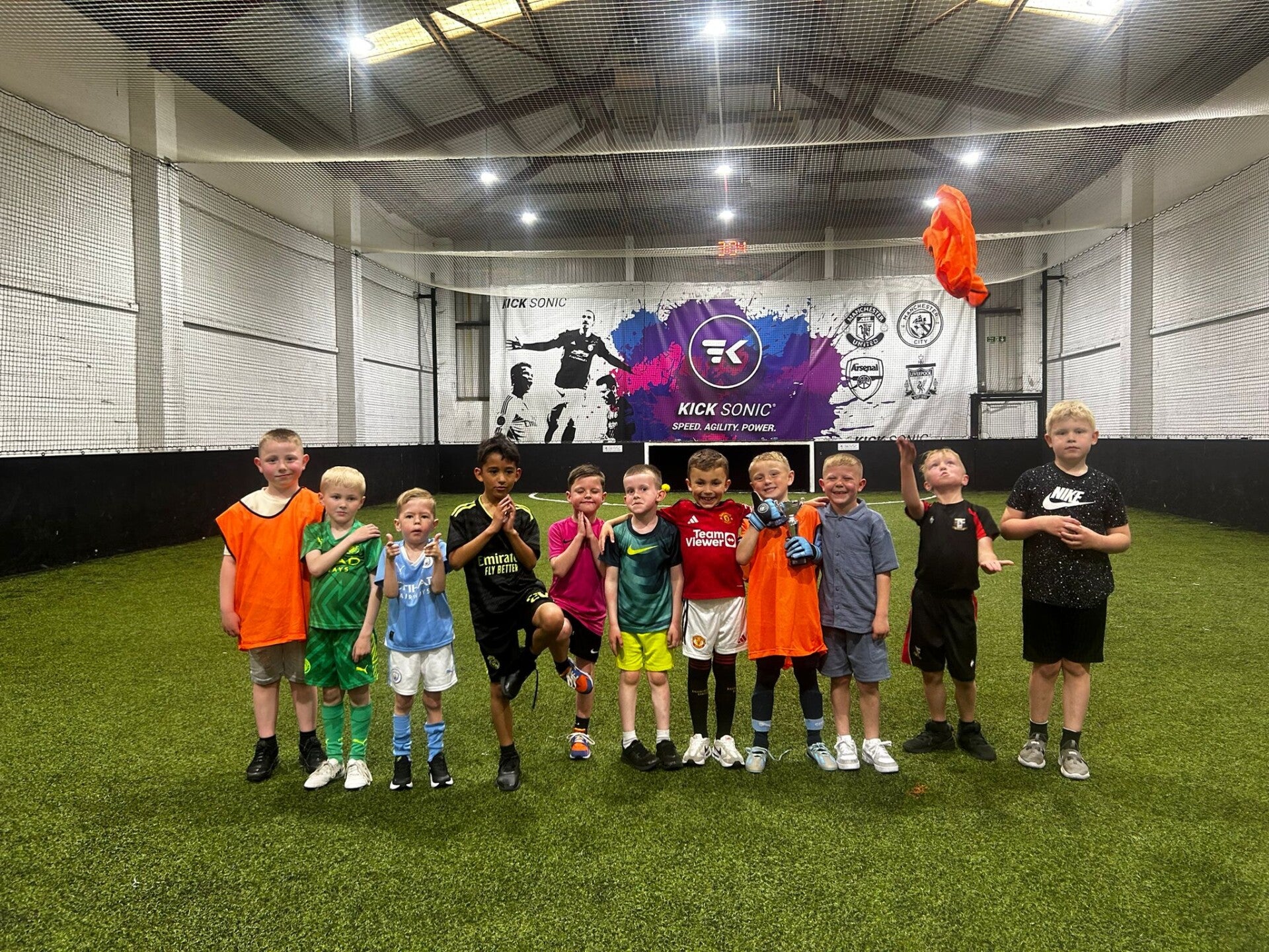 Indoor youth soccer event at KickSonic with kids in colorful jerseys, promoting teamwork.