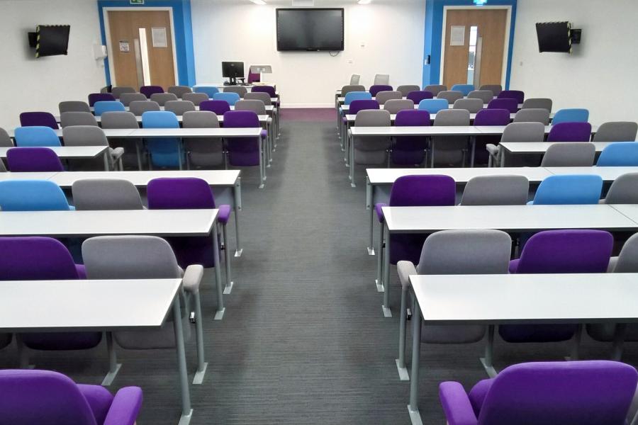 Modern workshop room at University of Law, Manchester, with colorful chairs and dual screens.