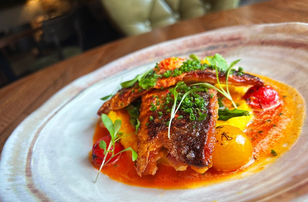 Seared fish dish with herbs and veggies, ideal for events and banquets.