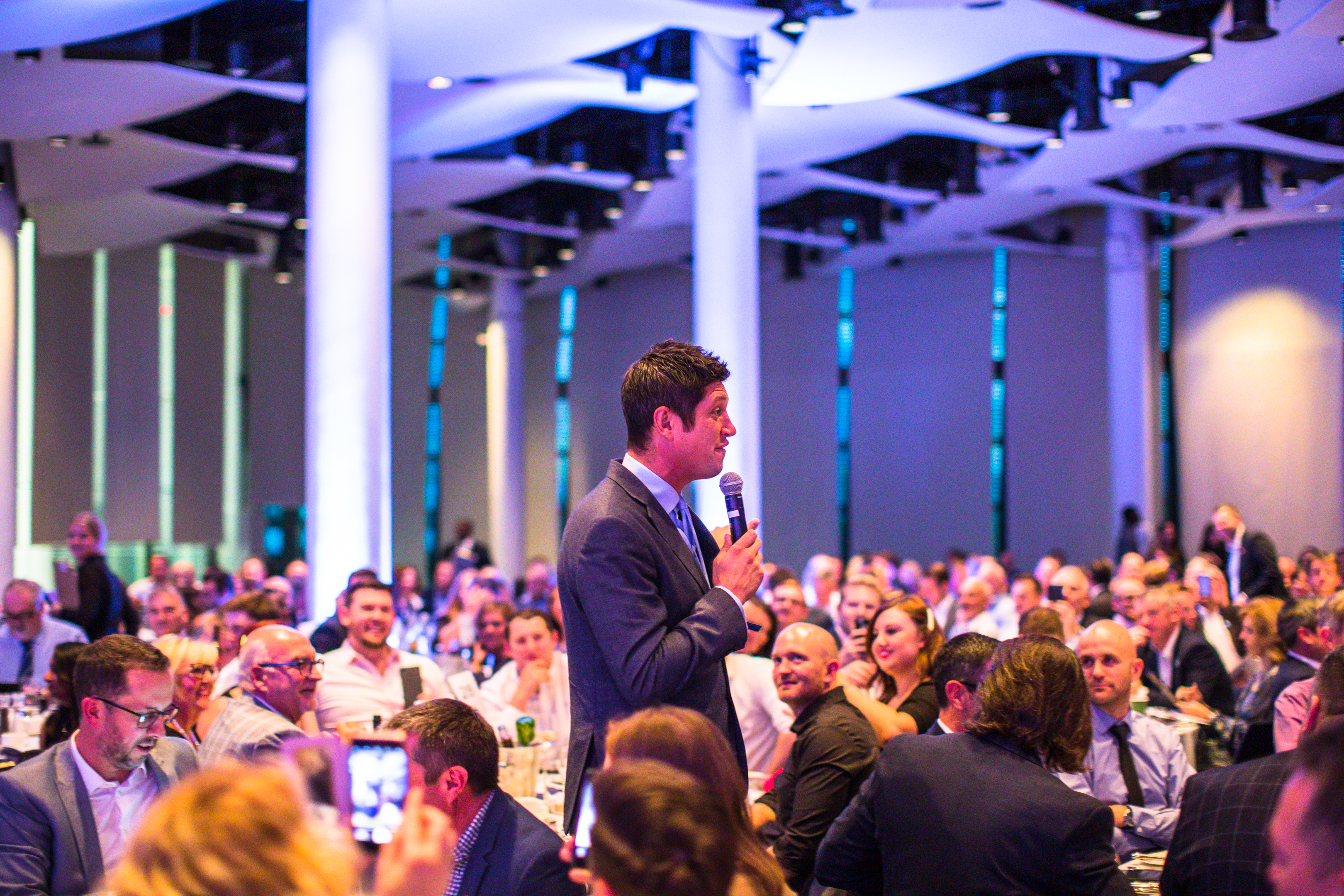 Great Hall at Wembley Stadium, speaker engaging audience, formal dinner event.