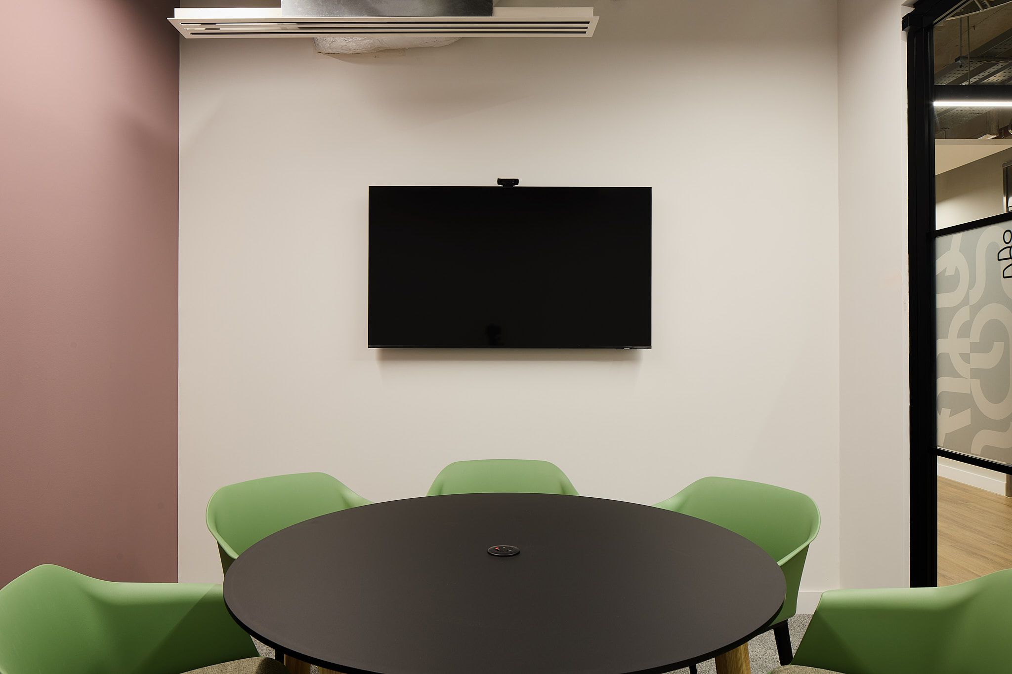 Modern meeting room with sleek black table and green chairs, ideal for conferences and workshops.