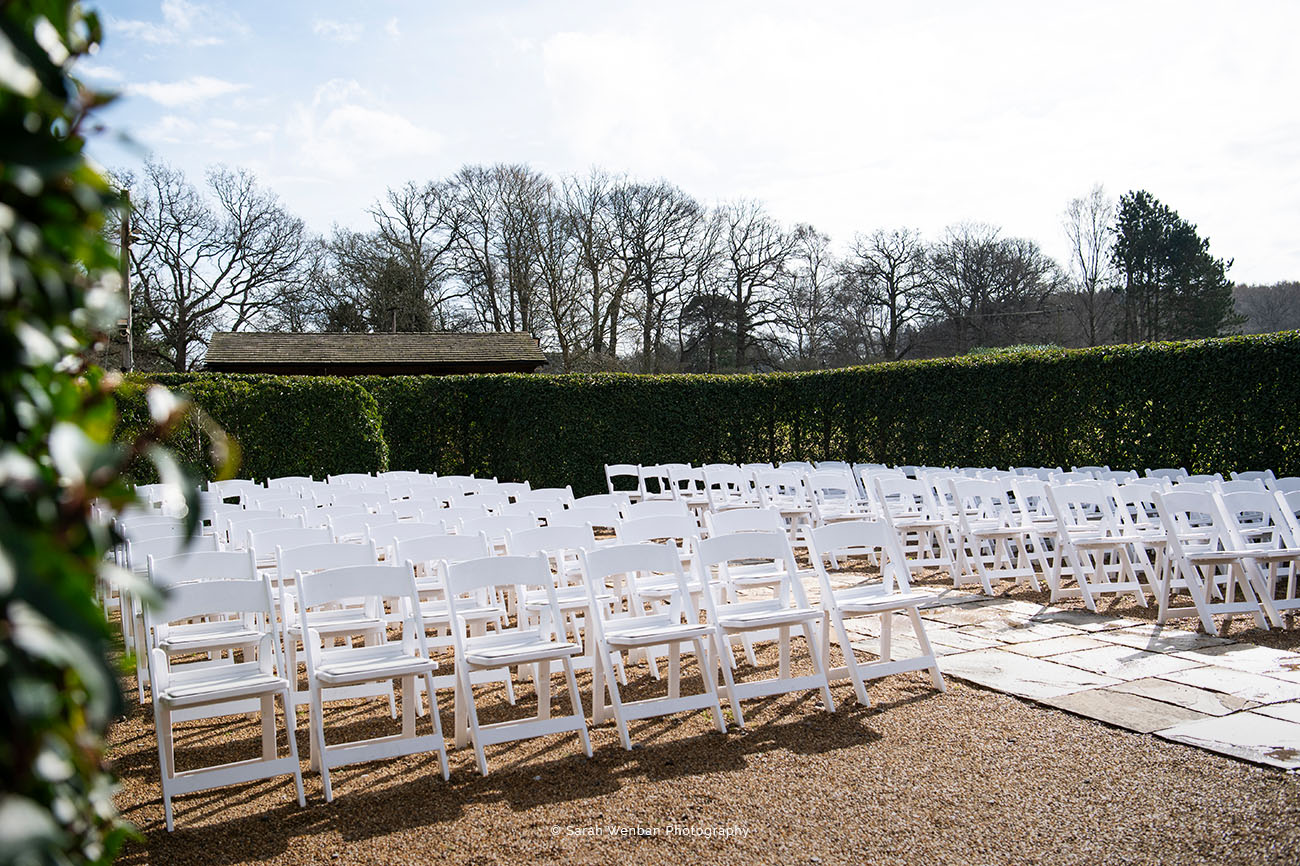 Outdoor garden wedding ceremony with white chairs and lush greenery at Brookfield Barn.