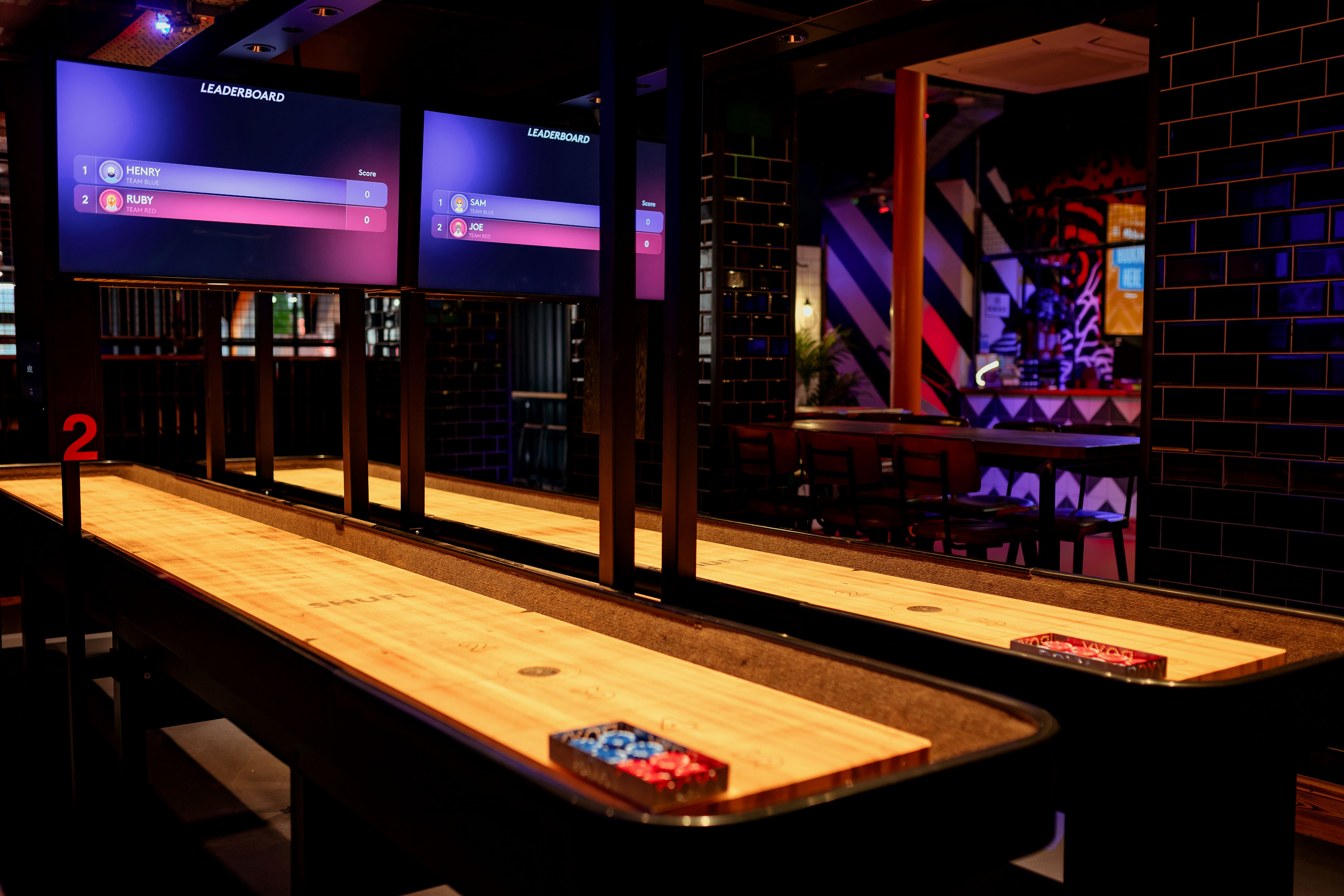 "Vibrant shuffleboard venue with digital scoreboards for team-building events."