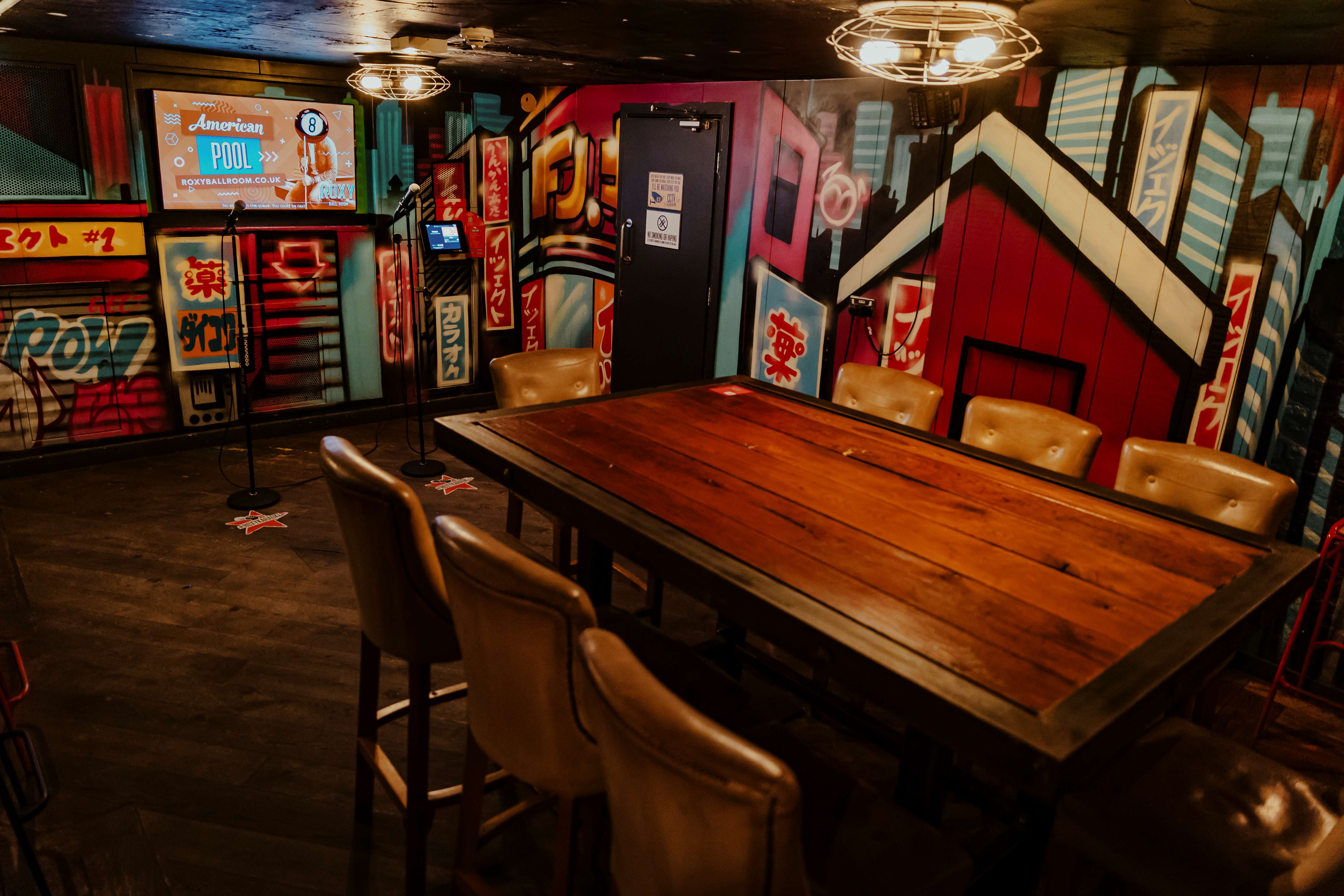 Karaoke room at Roxy Ball Room Leeds, featuring a rustic table and vibrant mural.