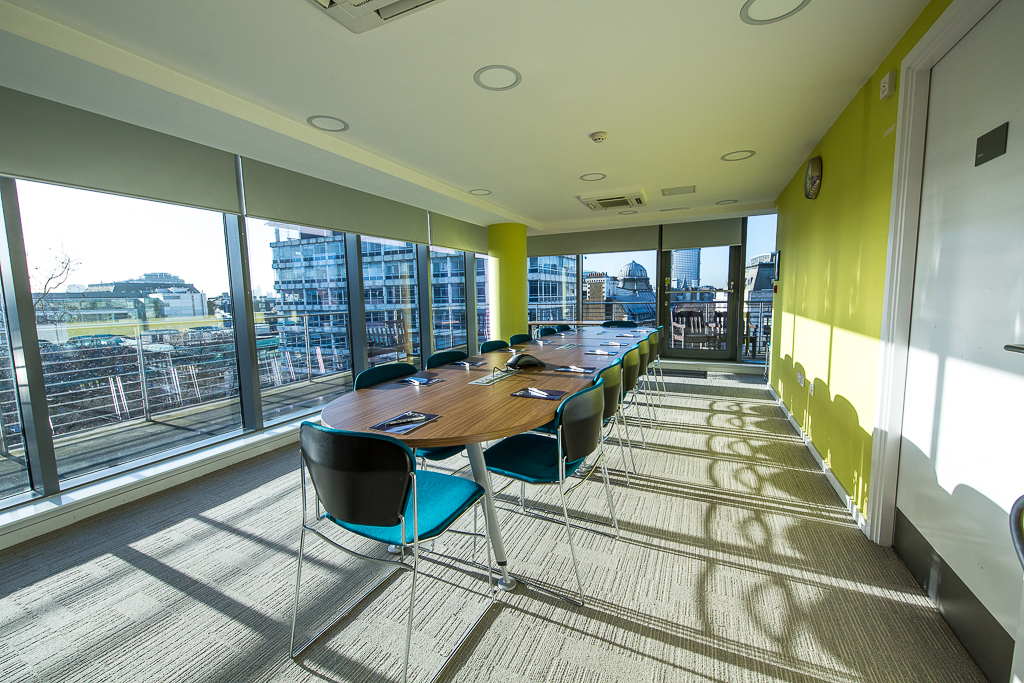 Modern meeting room with a long table and yellow walls, ideal for workshops and collaborations.
