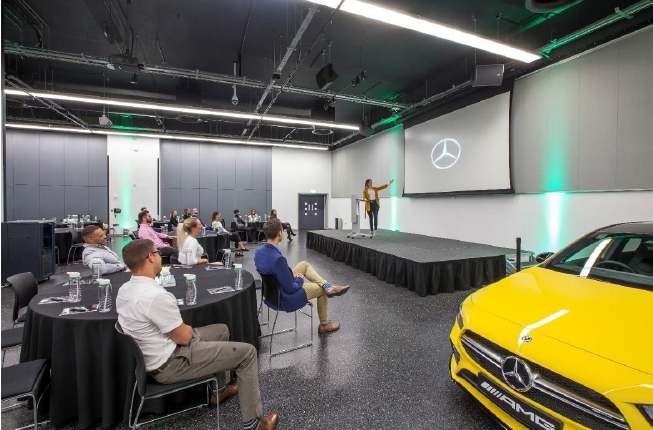 Brooklands Hall event space with stage, round tables, and luxury Mercedes for corporate presentations.
