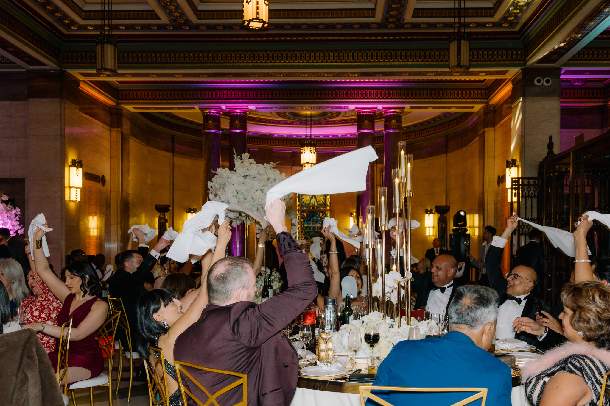Alt text: Vibrant gala in The Long Room, guests cheer with napkins raised, elegant decor.