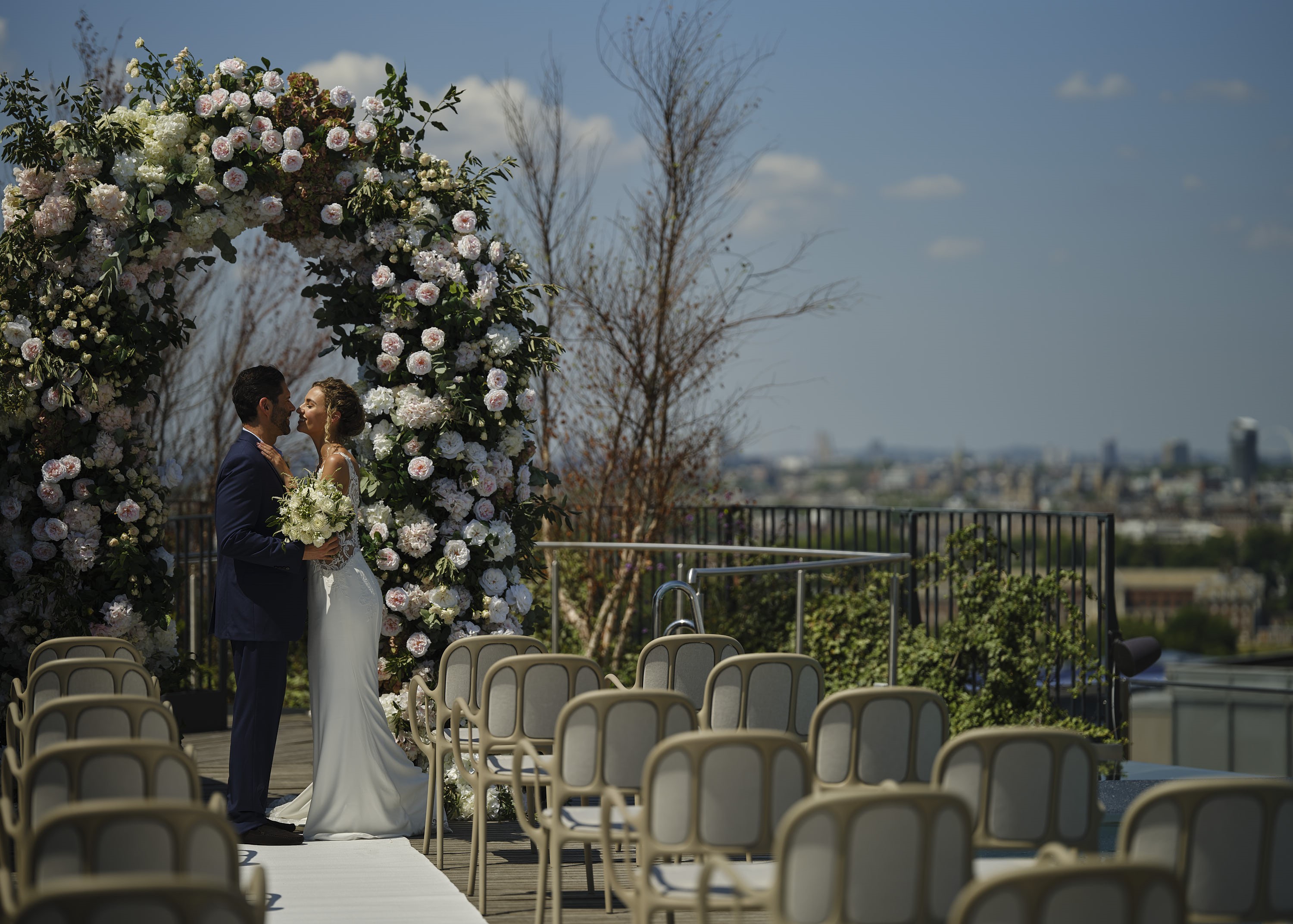 Outdoor wedding ceremony at art'otel London with floral arch and city skyline.