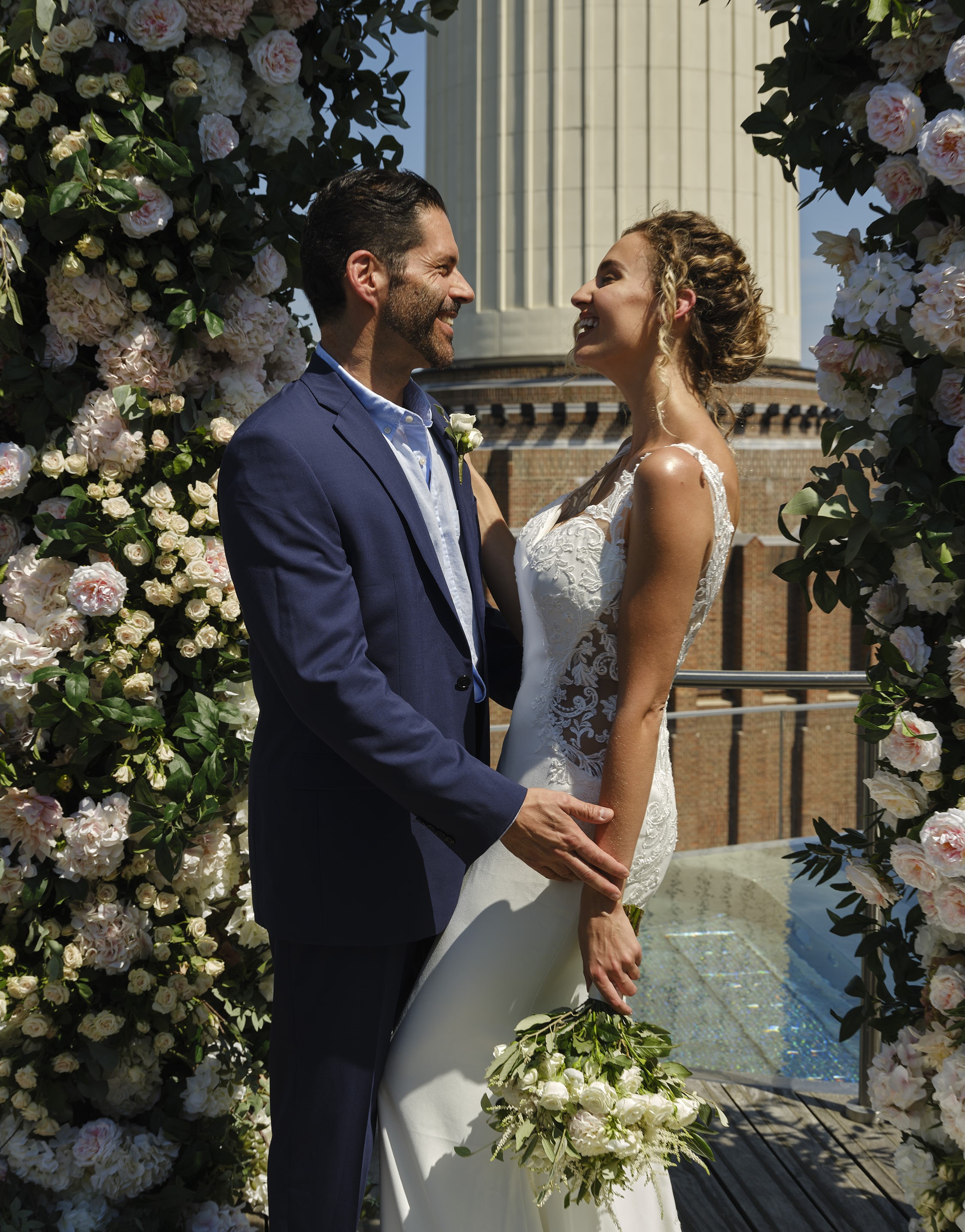 Couple exchanging vows under floral arch at JOIA Rooftop, London wedding venue.