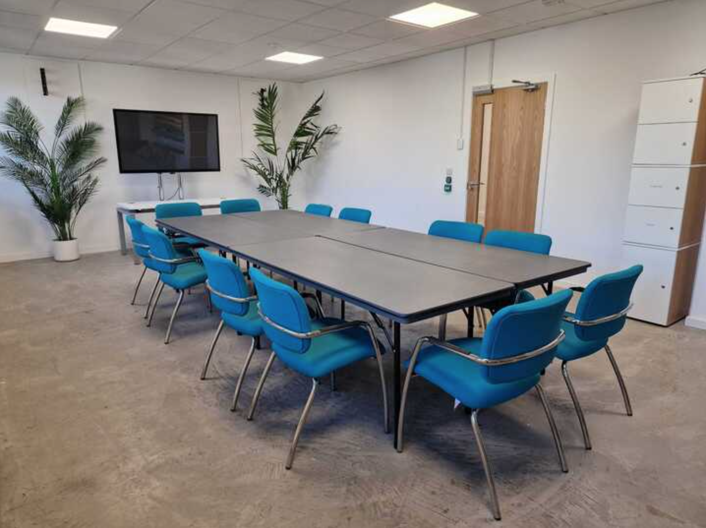 Modern meeting room in MAKE IT Barking, featuring a long table and vibrant blue chairs.