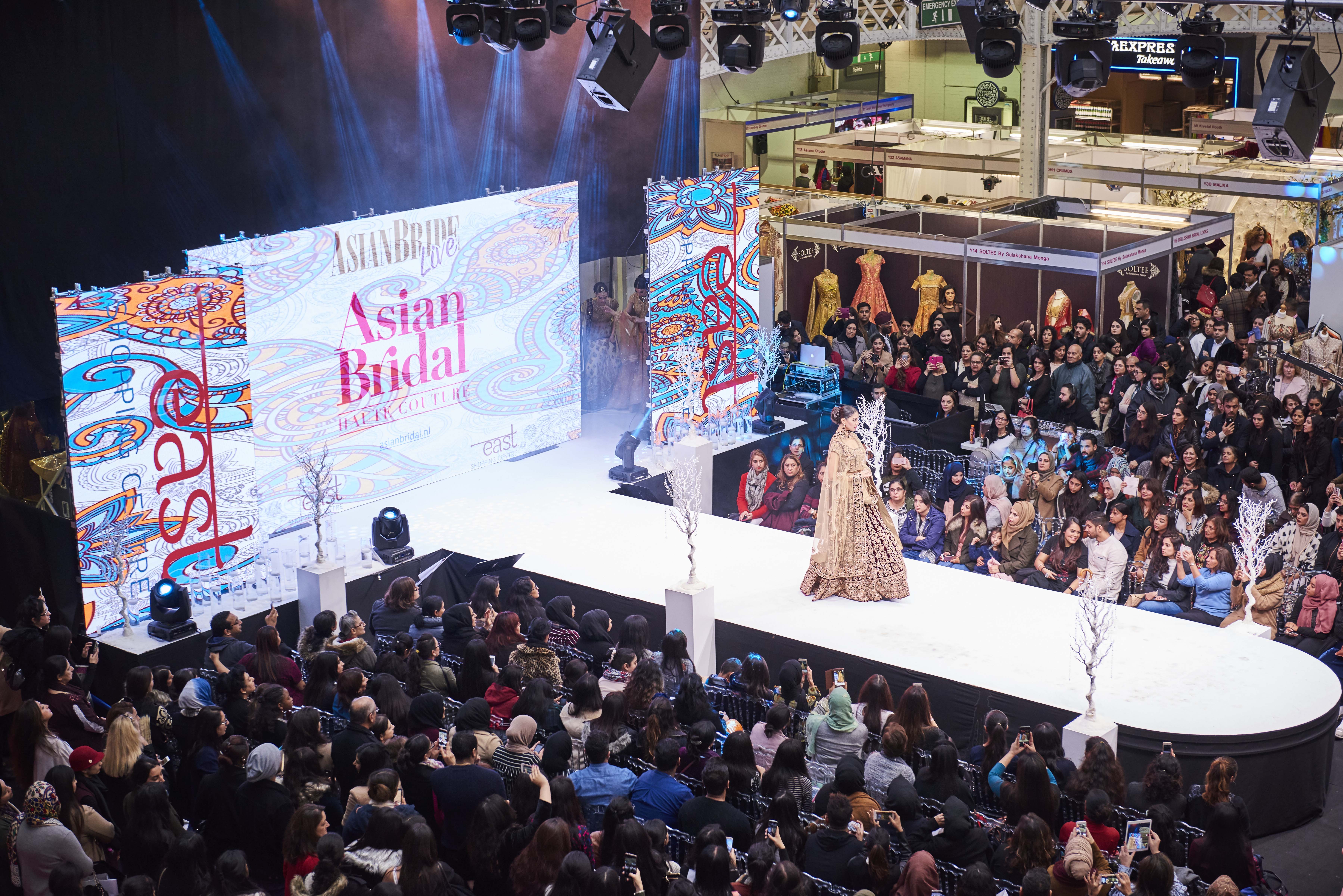 Fashion show at The National Hall in Olympia with vibrant runway and engaged audience.