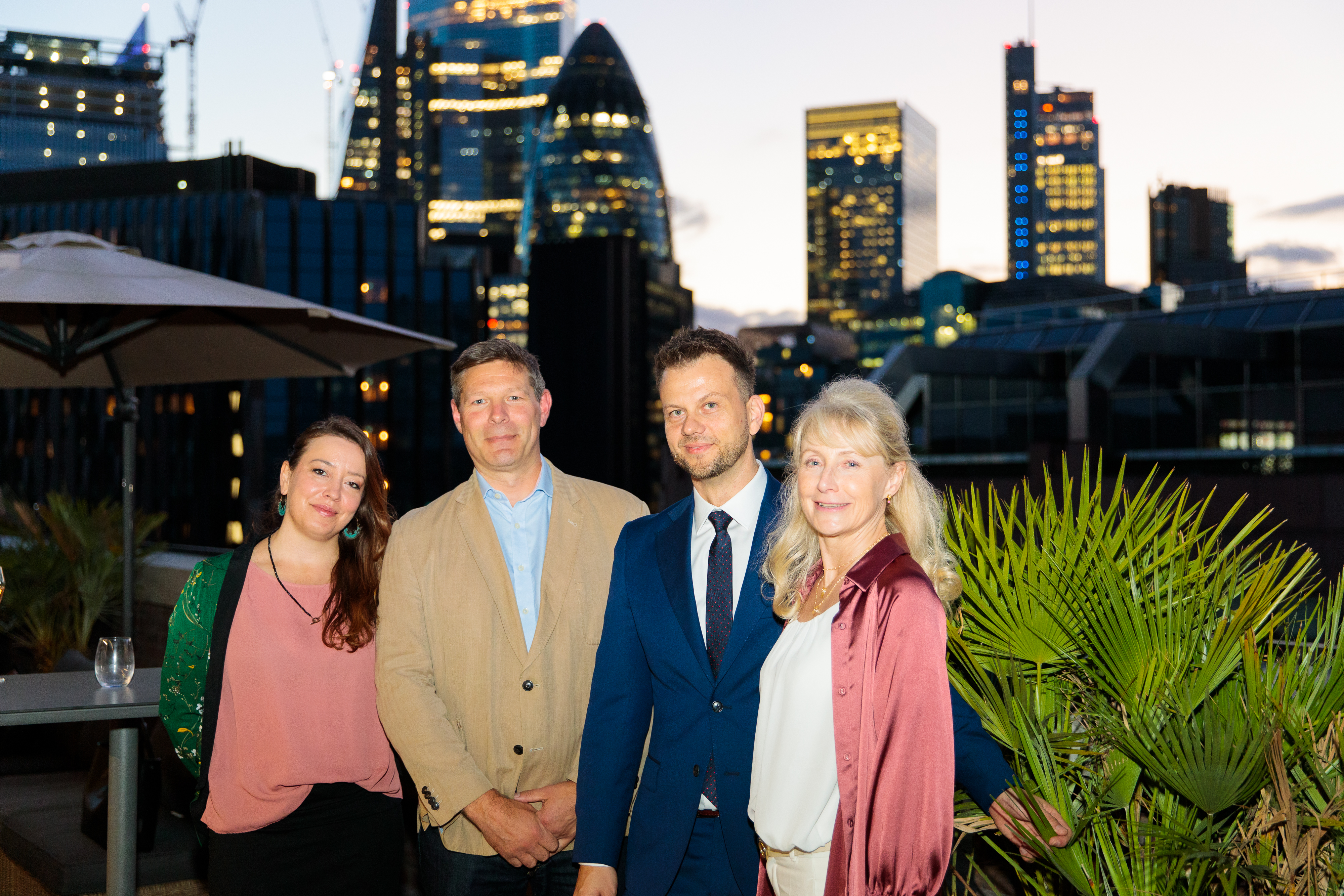 Summer rooftop party with professionals in business attire against a city skyline.