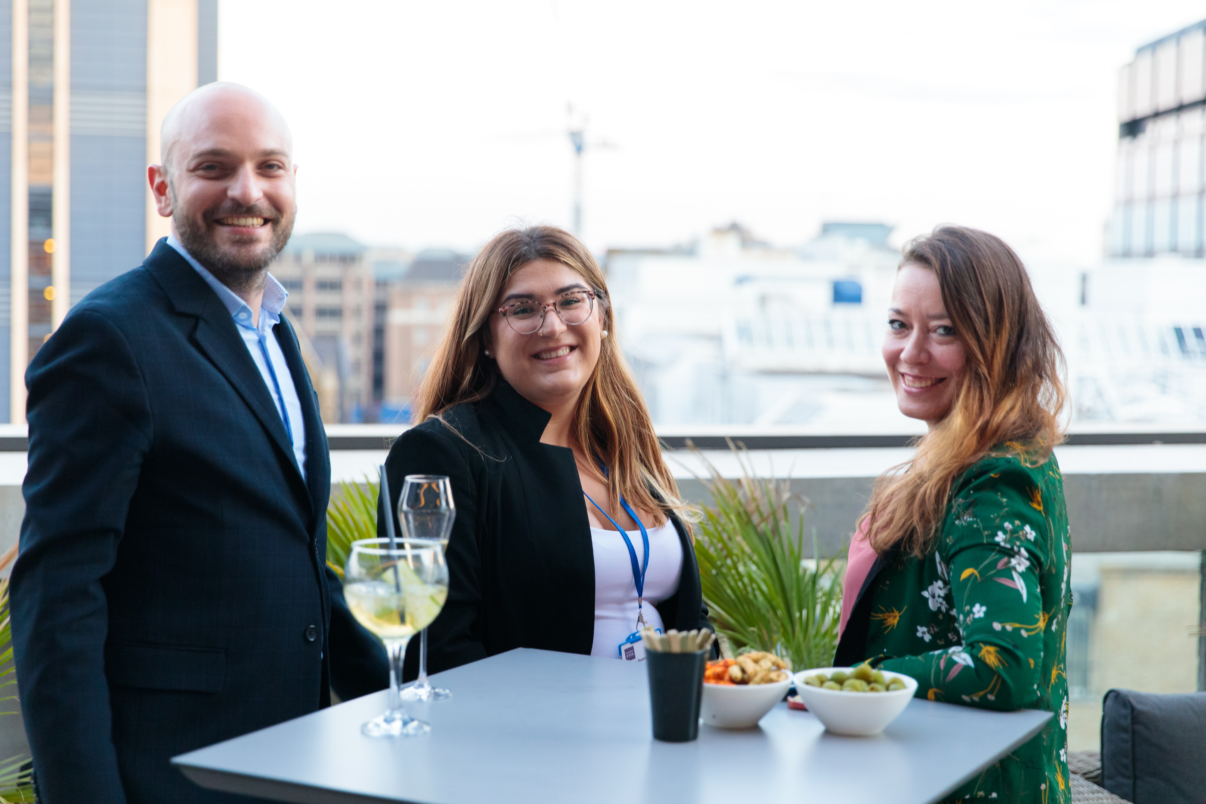 Summer rooftop party with professionals networking against a city skyline backdrop.
