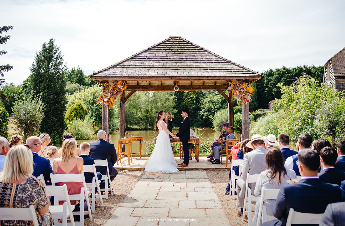 Outdoor wedding ceremony at Brookfield Barn with a gazebo by a serene pond.