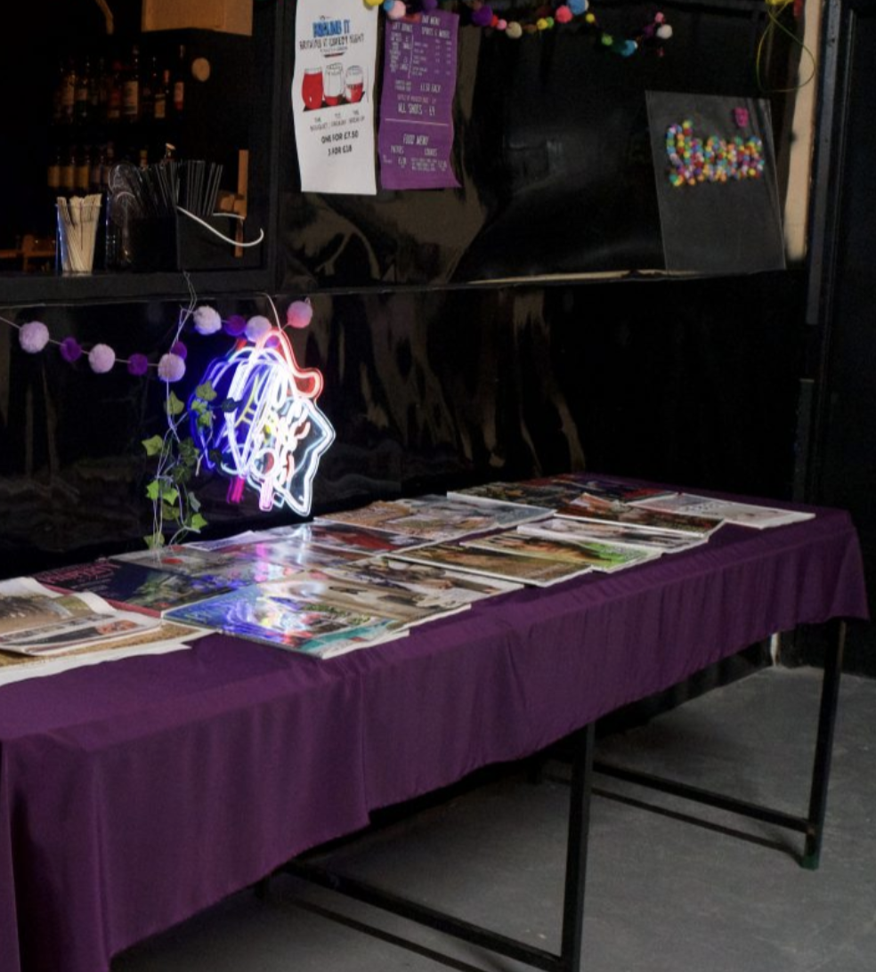 Messy venue display at Shaes London featuring disorganized marketing collateral and purple cloth.
