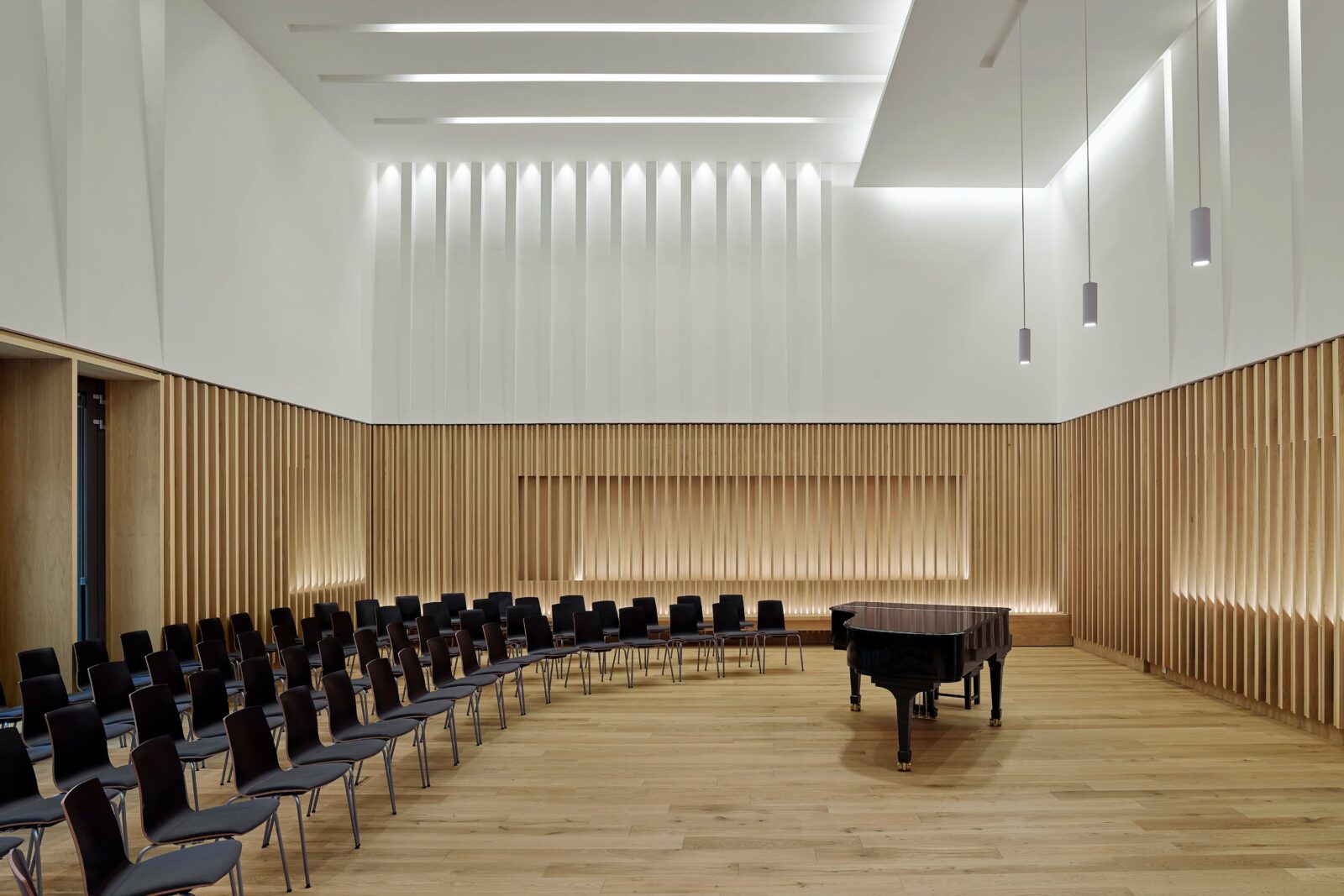 Modern rehearsal studio with curved chairs around a grand piano, ideal for workshops.