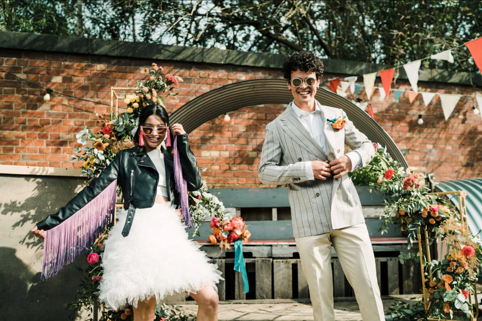 Stylish couple at vibrant outdoor wedding venue with colorful floral arrangements.