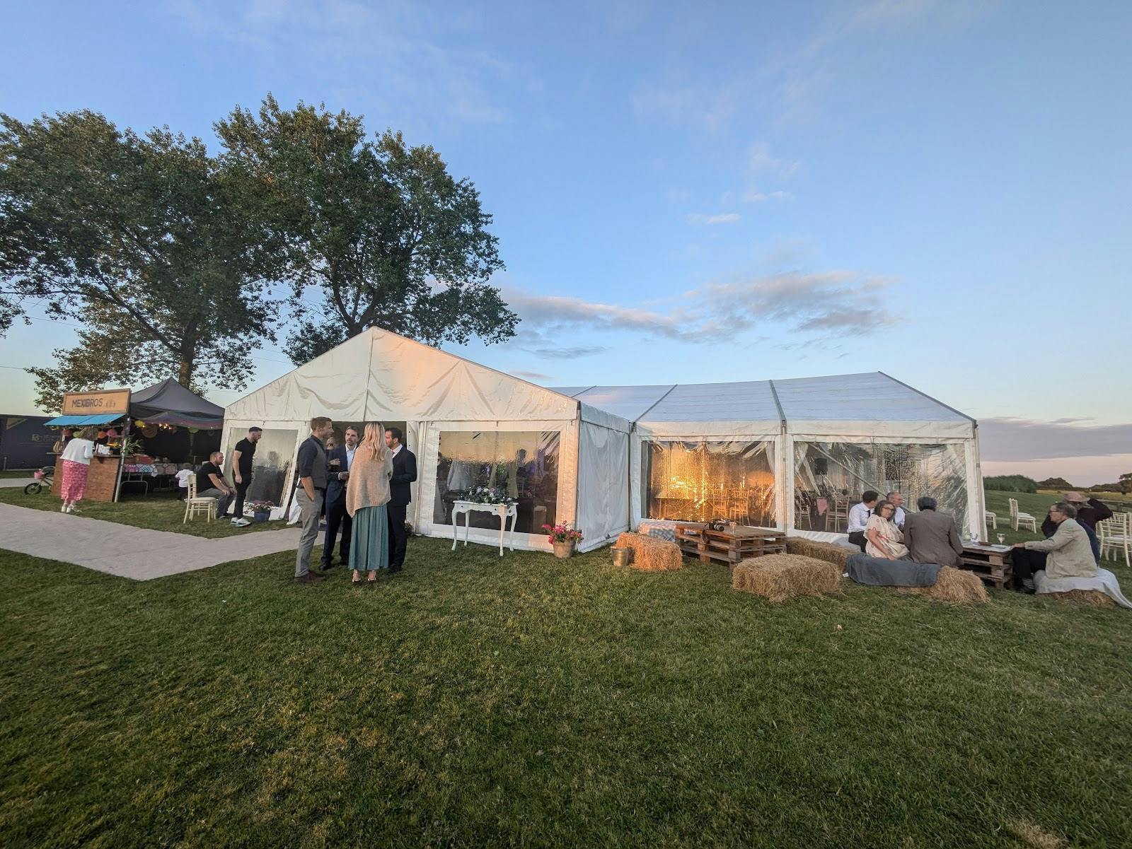 Rustic barn conversion outdoor marquee event with hay bale seating for high-end wedding parties.