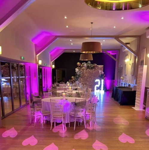 Rustic event space at Redlibbets Golf Club with purple uplighting and rose-gold party backdrop.