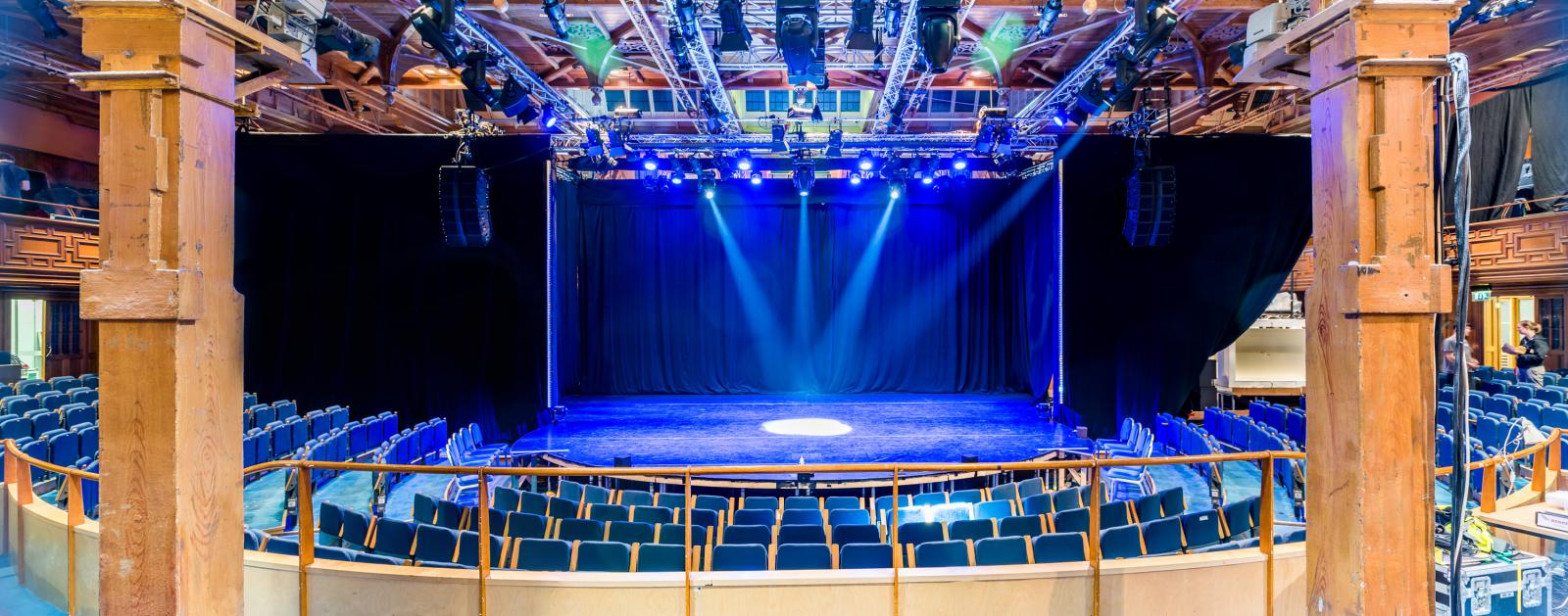 Assembly Hall proscenium stage with overhead lighting for keynote sessions and panel discussions.