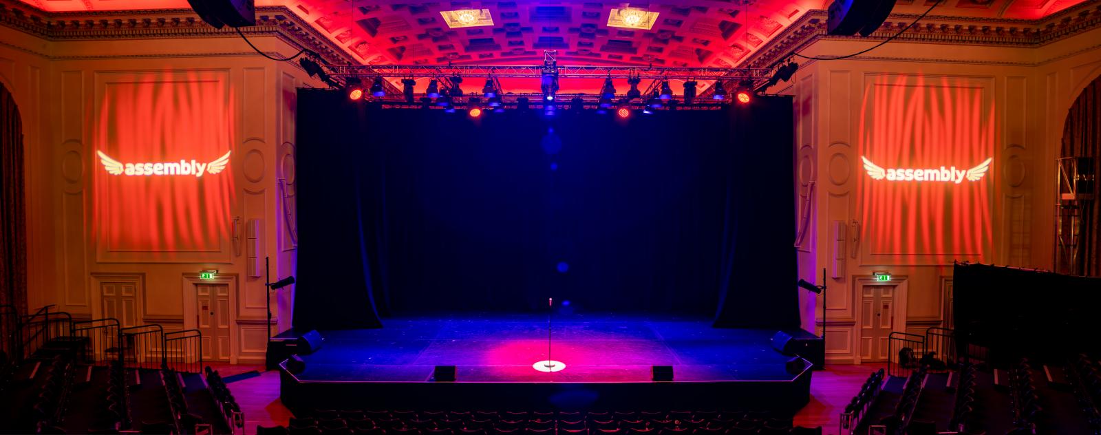 Assembly Hall stage with dramatic downstage lighting for keynote presentation and event venue.