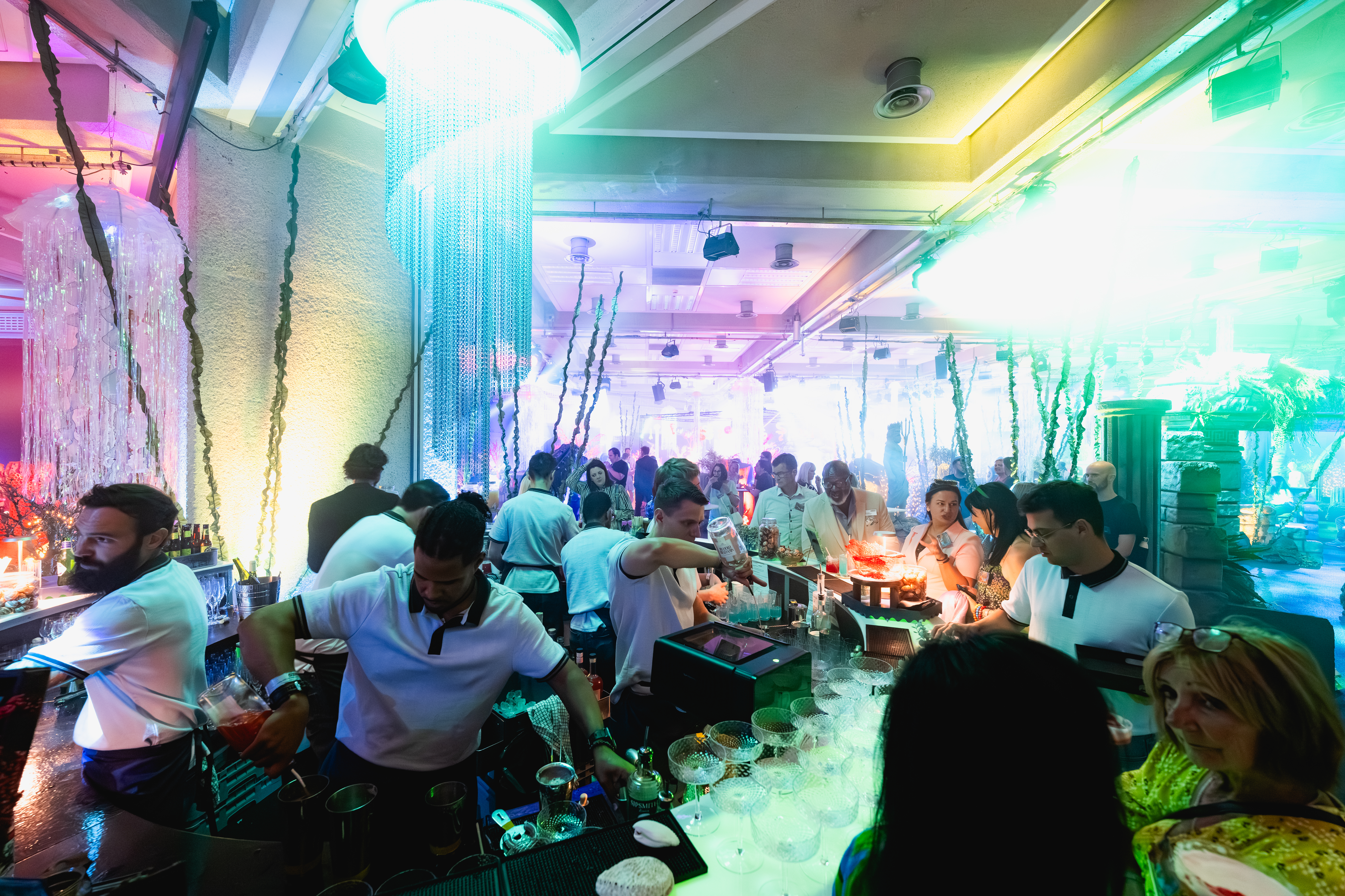 Vibrant networking event at QEII Centre with skilled bartenders in colorful lighting.