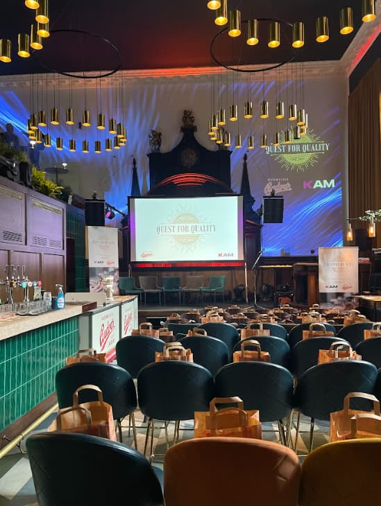 Full venue event space with green chairs and stage for "Quest for Quality" presentations.