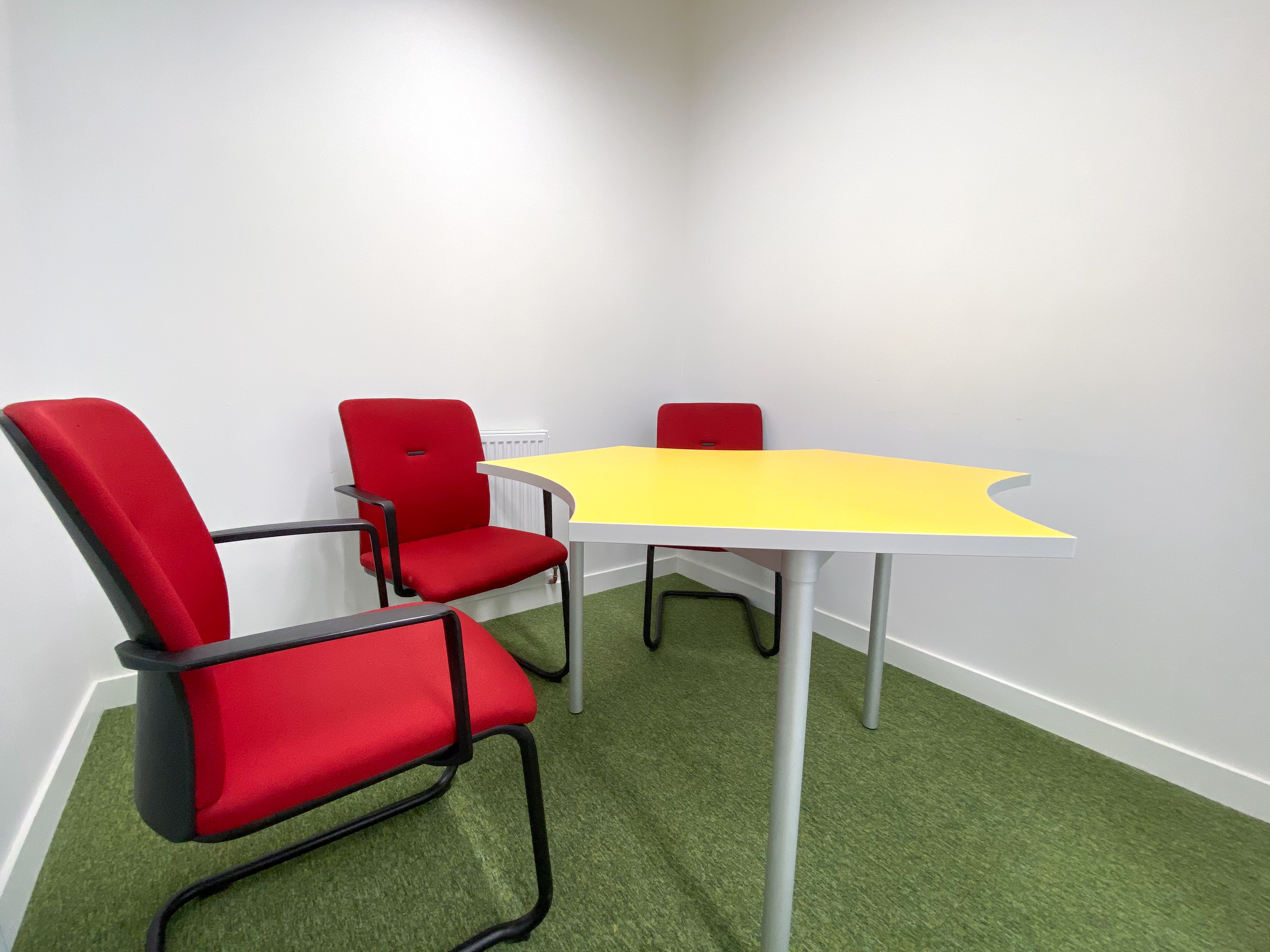 Modern consultation room with yellow table and red chairs, perfect for brainstorming sessions.