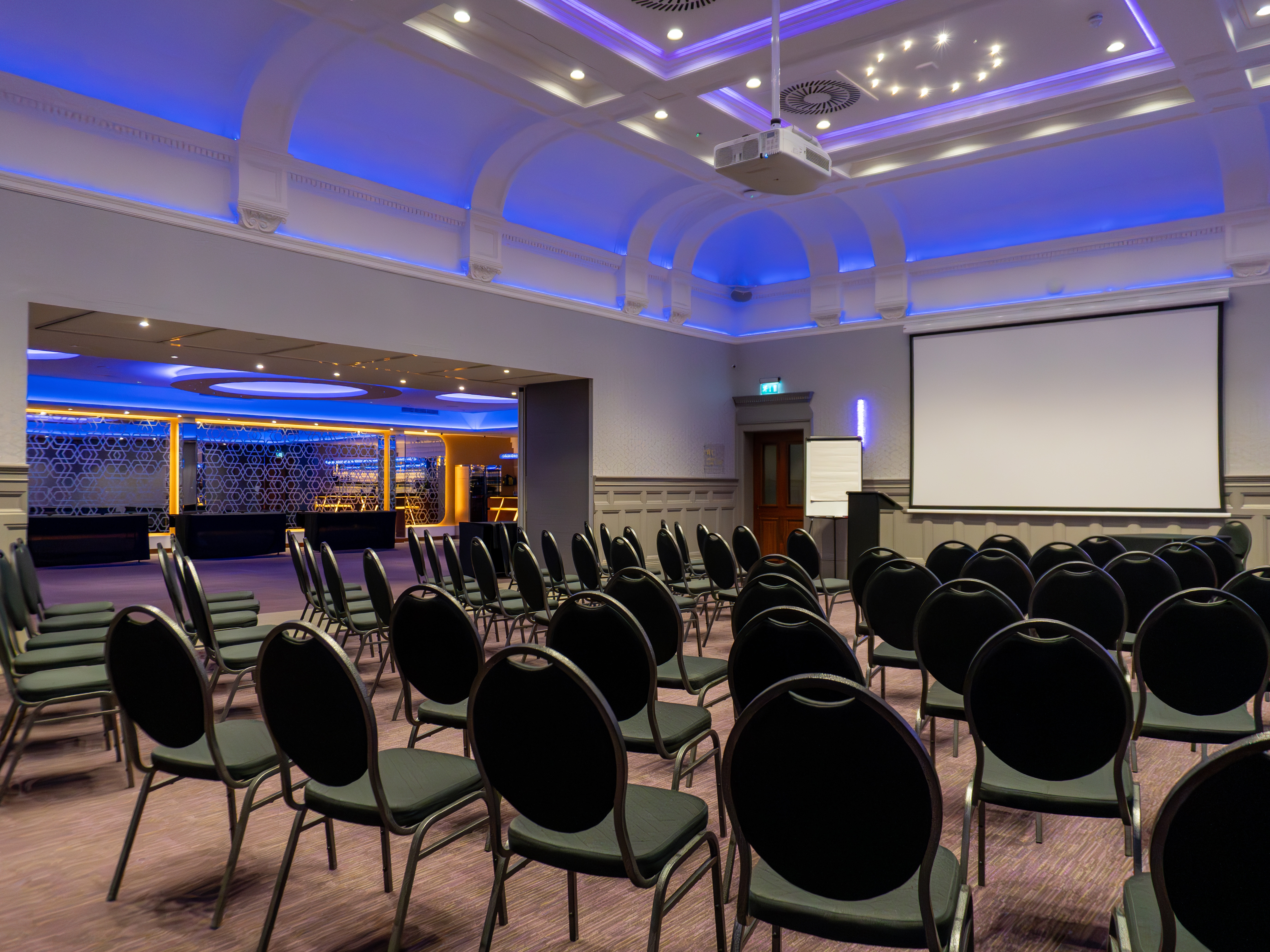 Event space at The Broughton, featuring black chairs and blue lighting for presentations.