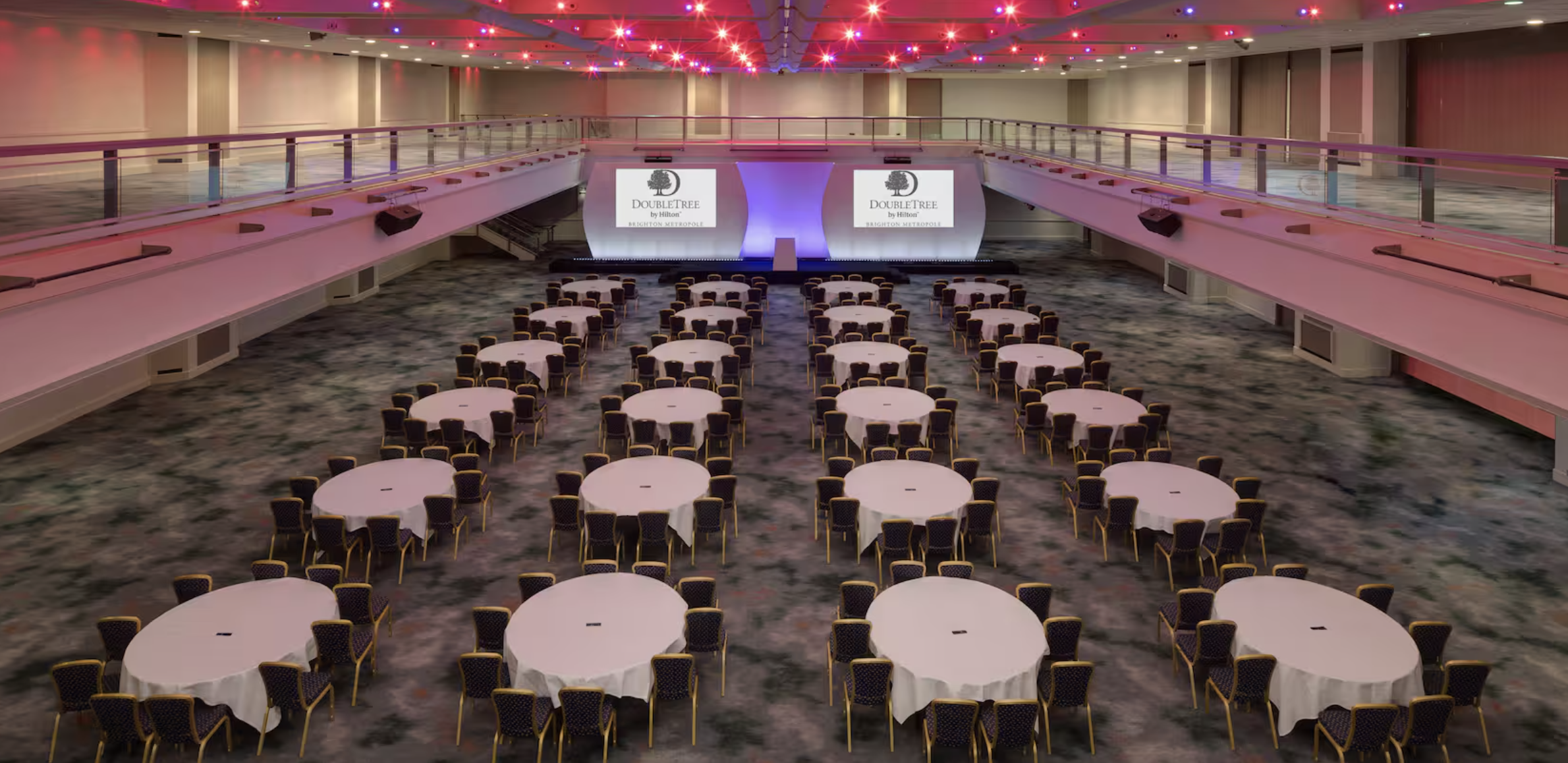 Spacious conference venue at DoubleTree Brighton with round tables and dynamic lighting.