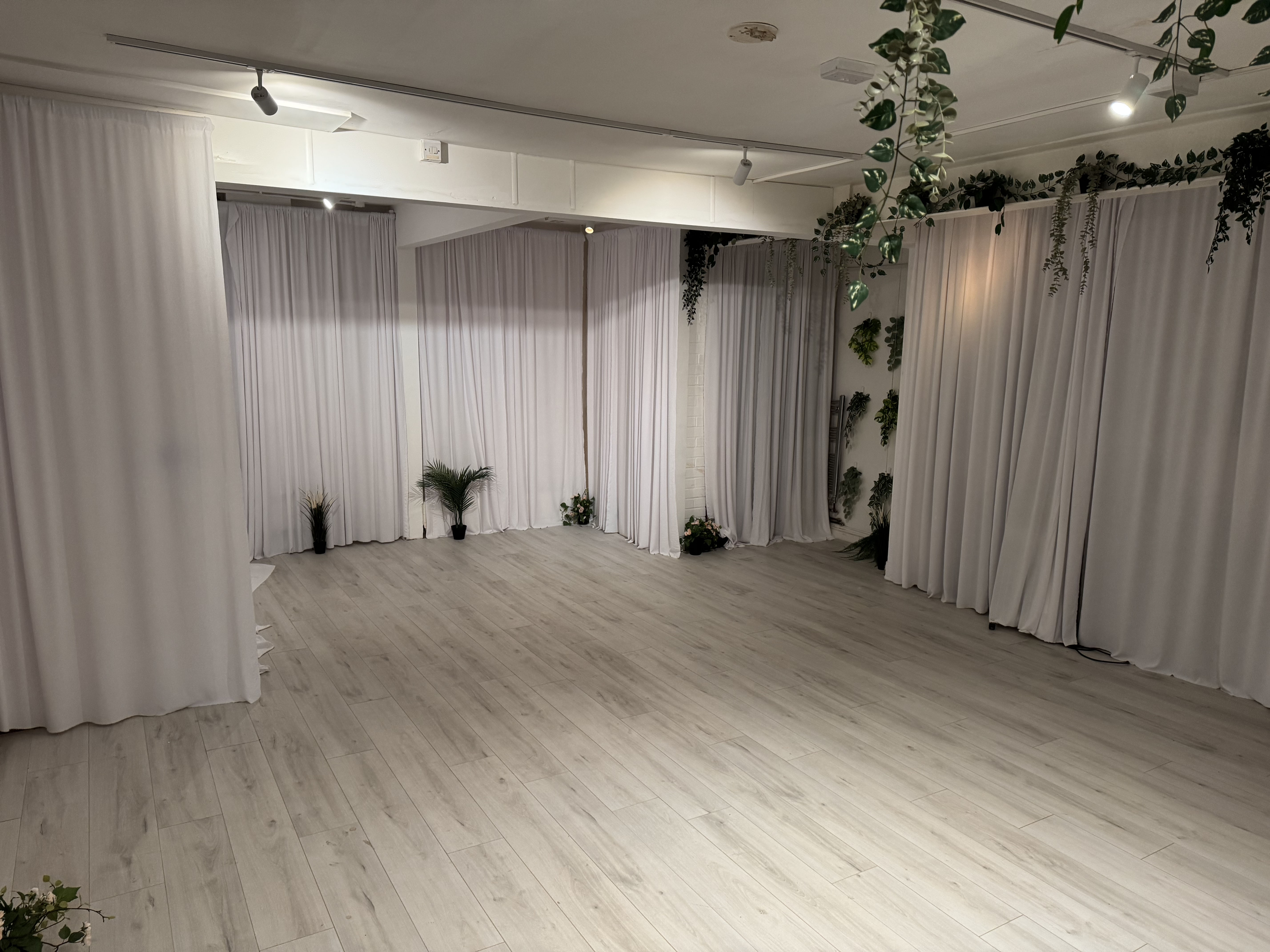 Minimalist studio event space with white drapery and wood floors for weddings and corporate events.