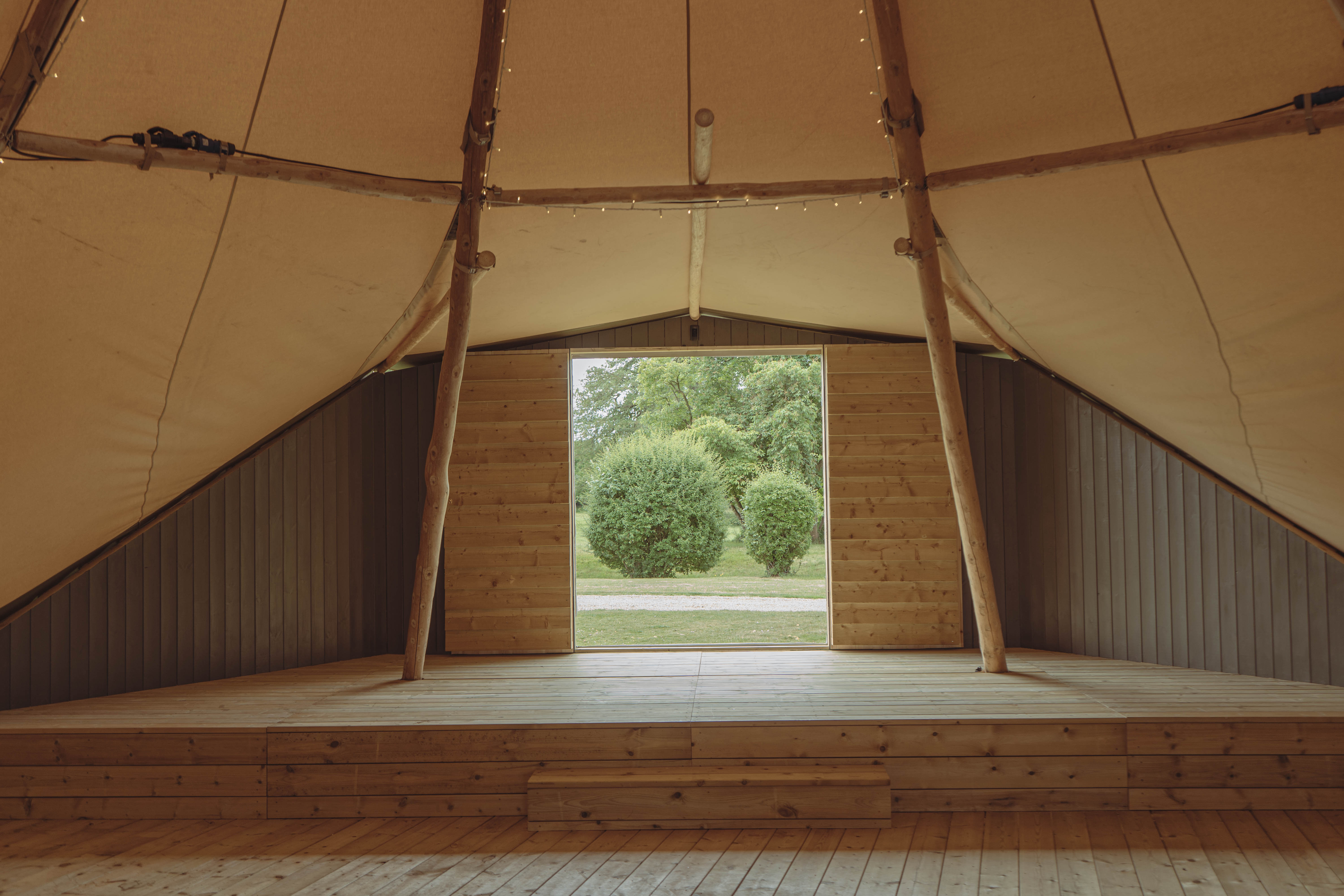 Rustic tipi venue for outdoor events, featuring wooden stage for brand activations and gatherings.
