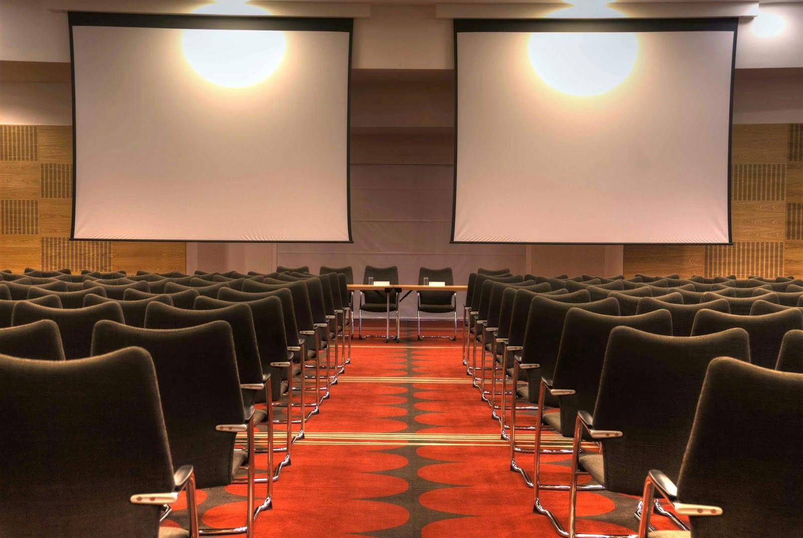 Plenary room theater layout with stage and dual screens for corporate conference event.