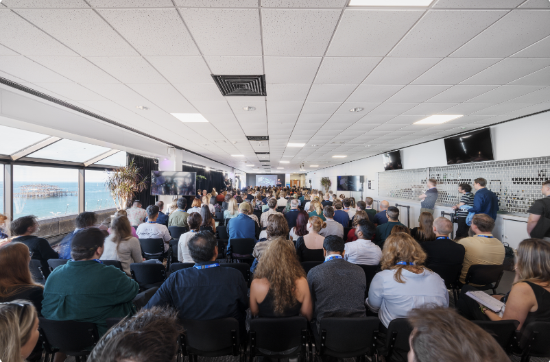 Brighton Centre conference with large audience and scenic waterfront backdrop.