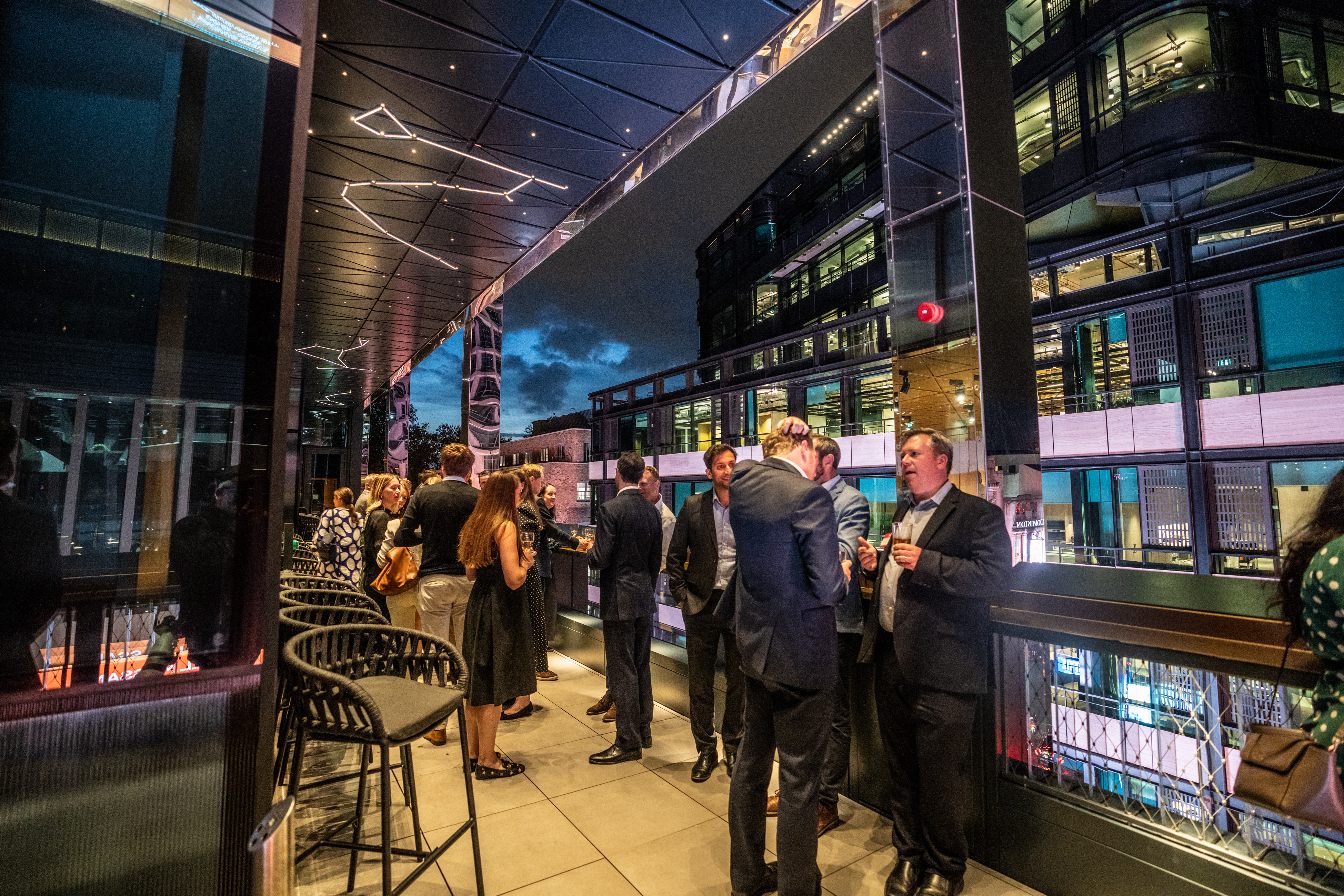 Evening networking event at Nica's Bar rooftop terrace, sleek architecture and city skyline.