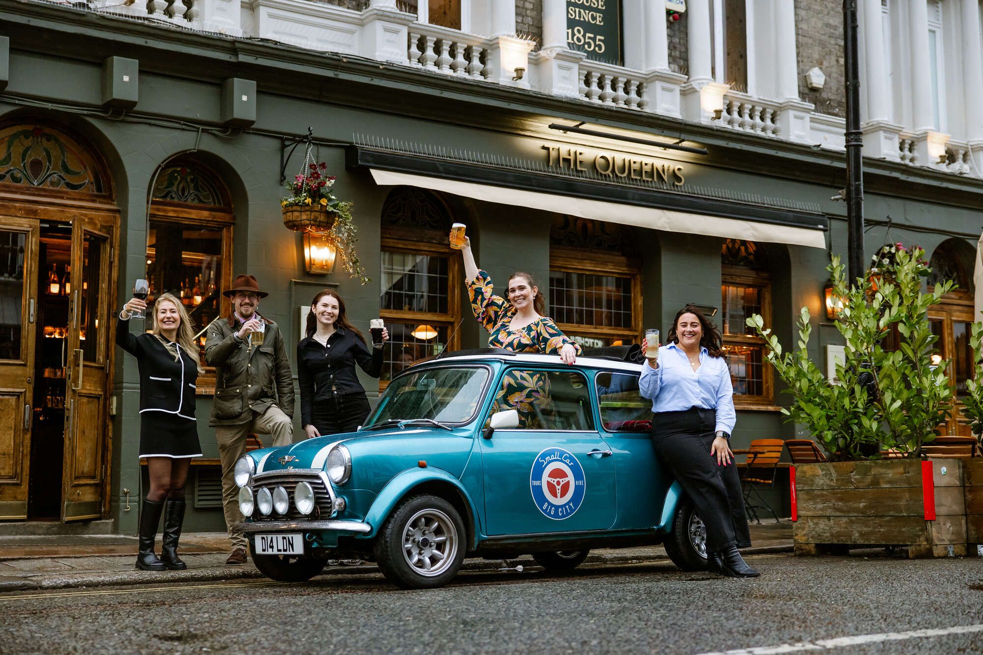 Promotional event at Queen's Quarters with vintage car and themed attire, perfect for gatherings.