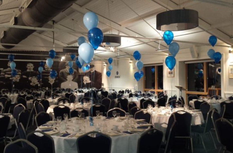 Banquet-style social event at Lansdowne FC featuring blue balloon centerpieces in industrial venue.