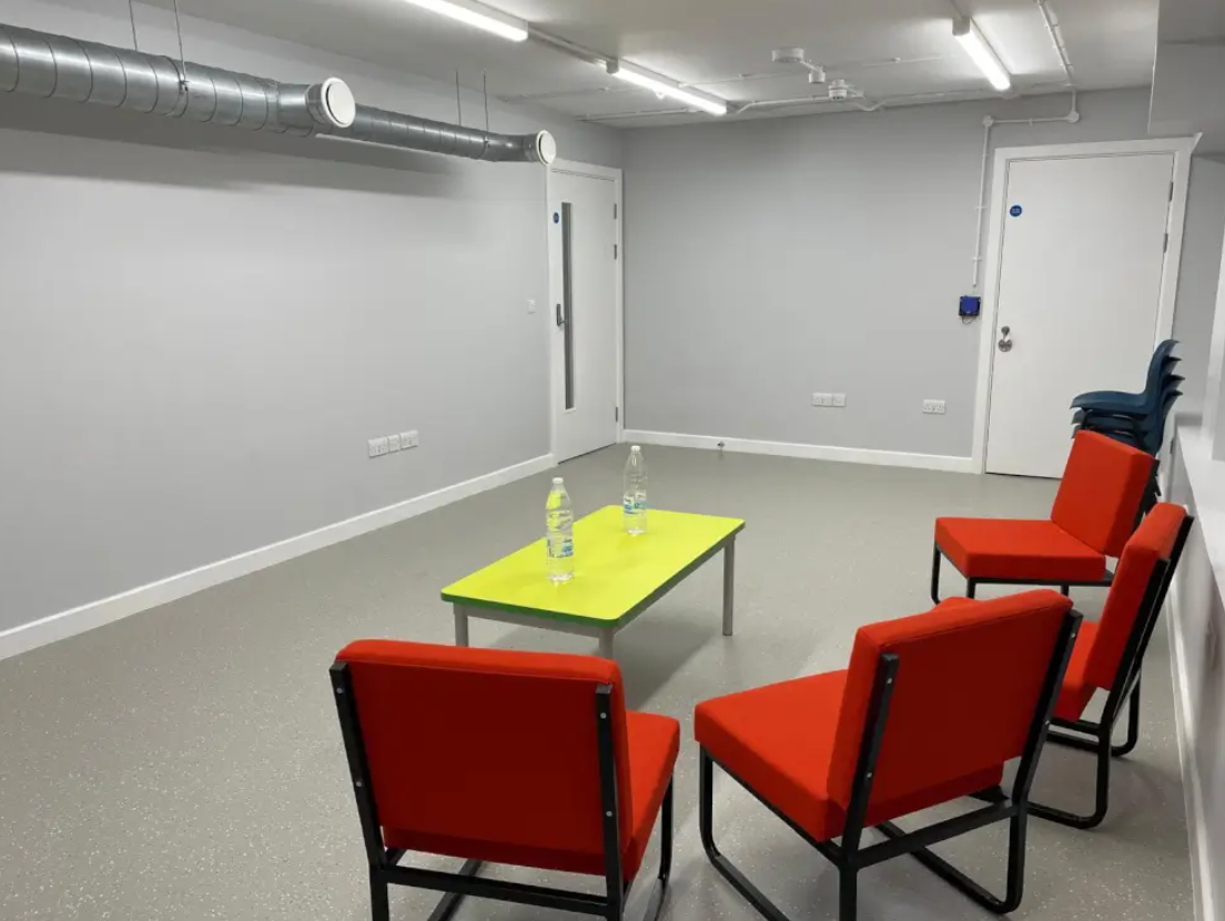 Alt text: Queen Adelaide meeting space with red chairs and a green table for workshops.