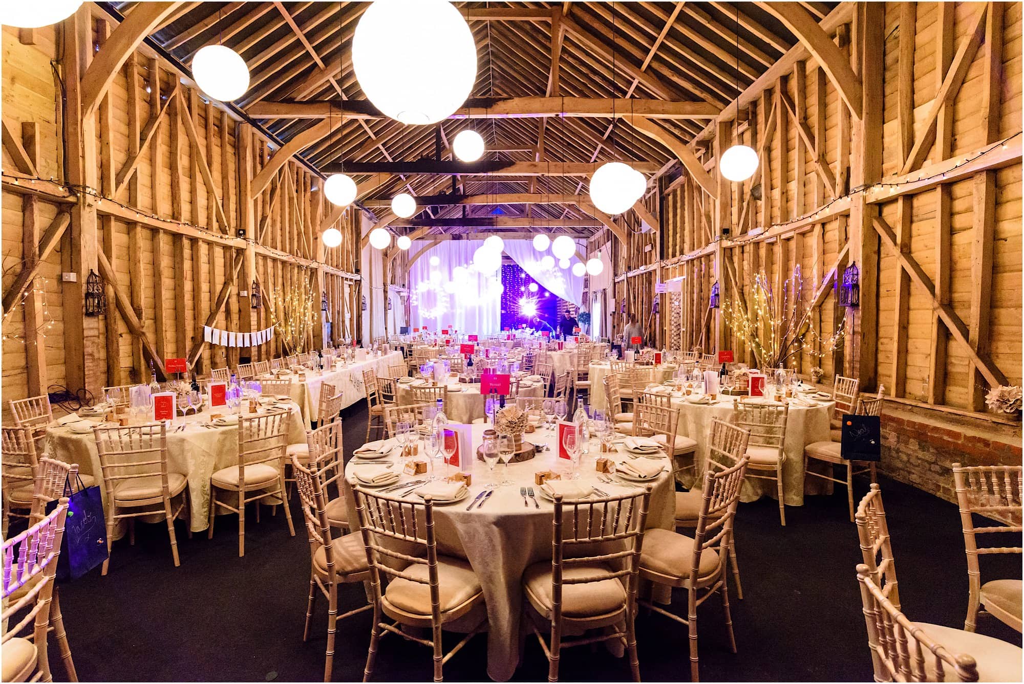 Rustic-chic Long Barn venue with timber frames and round tables for formal wedding events.