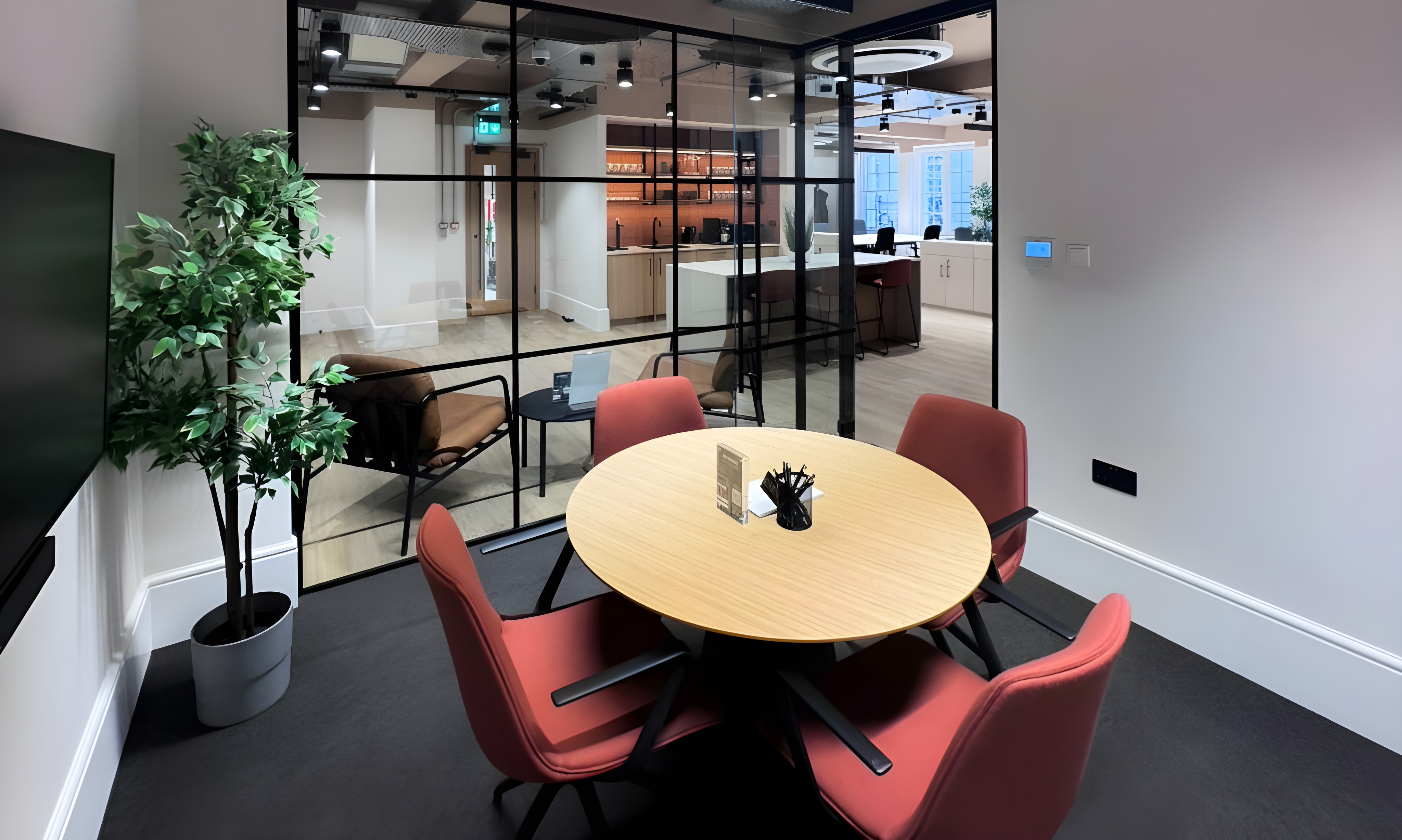 Modern collaborative meeting space with round table, glass walls, ideal for teamwork and brainstorming.