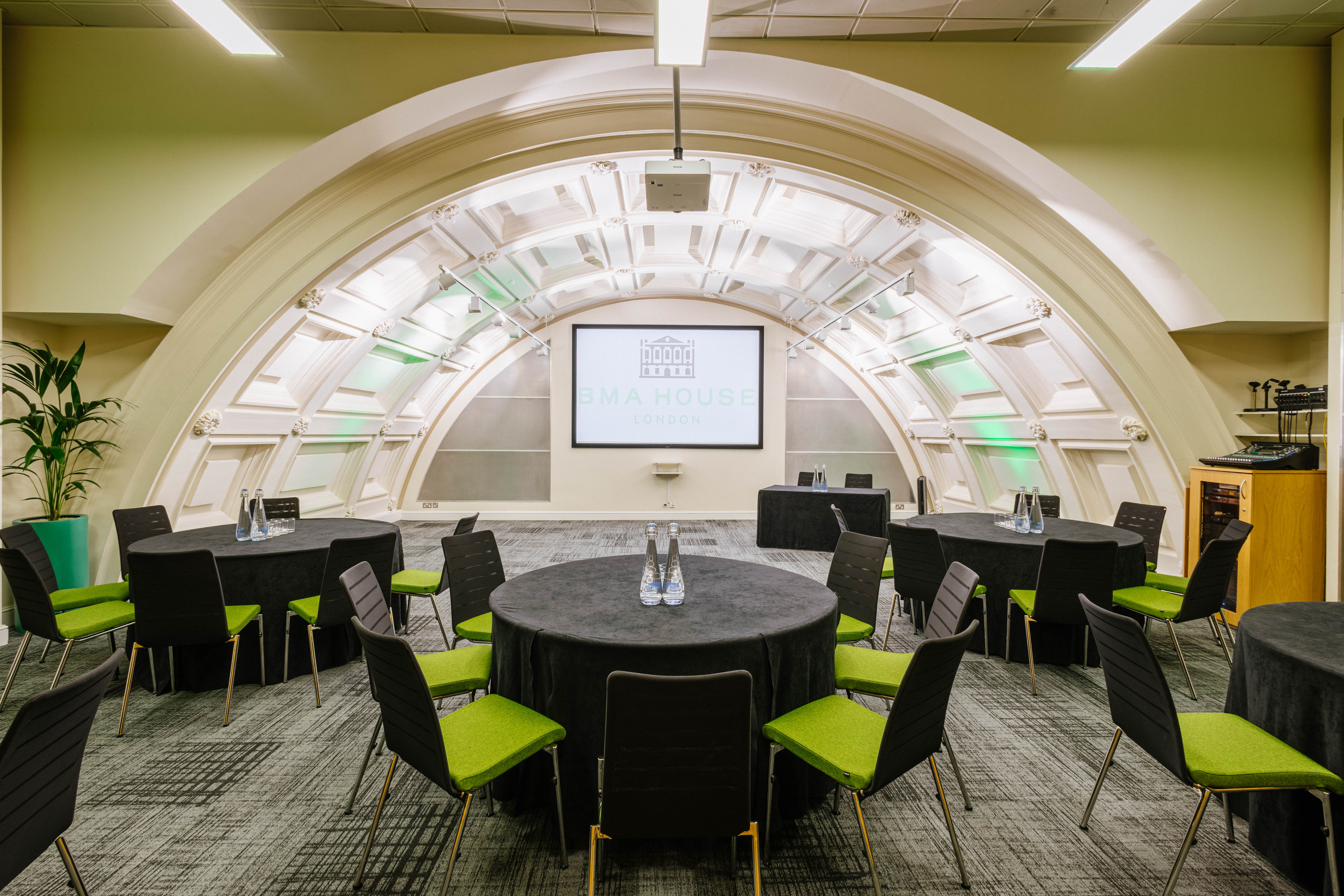 Low-Impact DDR event space with round tables and green chairs, ideal for workshops or meetings.
