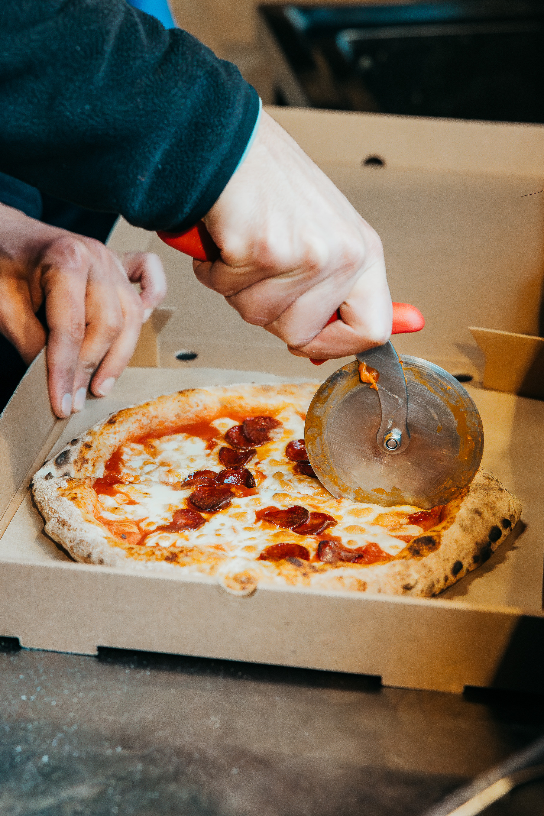 Hand using a pizza cutter on pepperoni pizza at Flat Iron Square event catering.