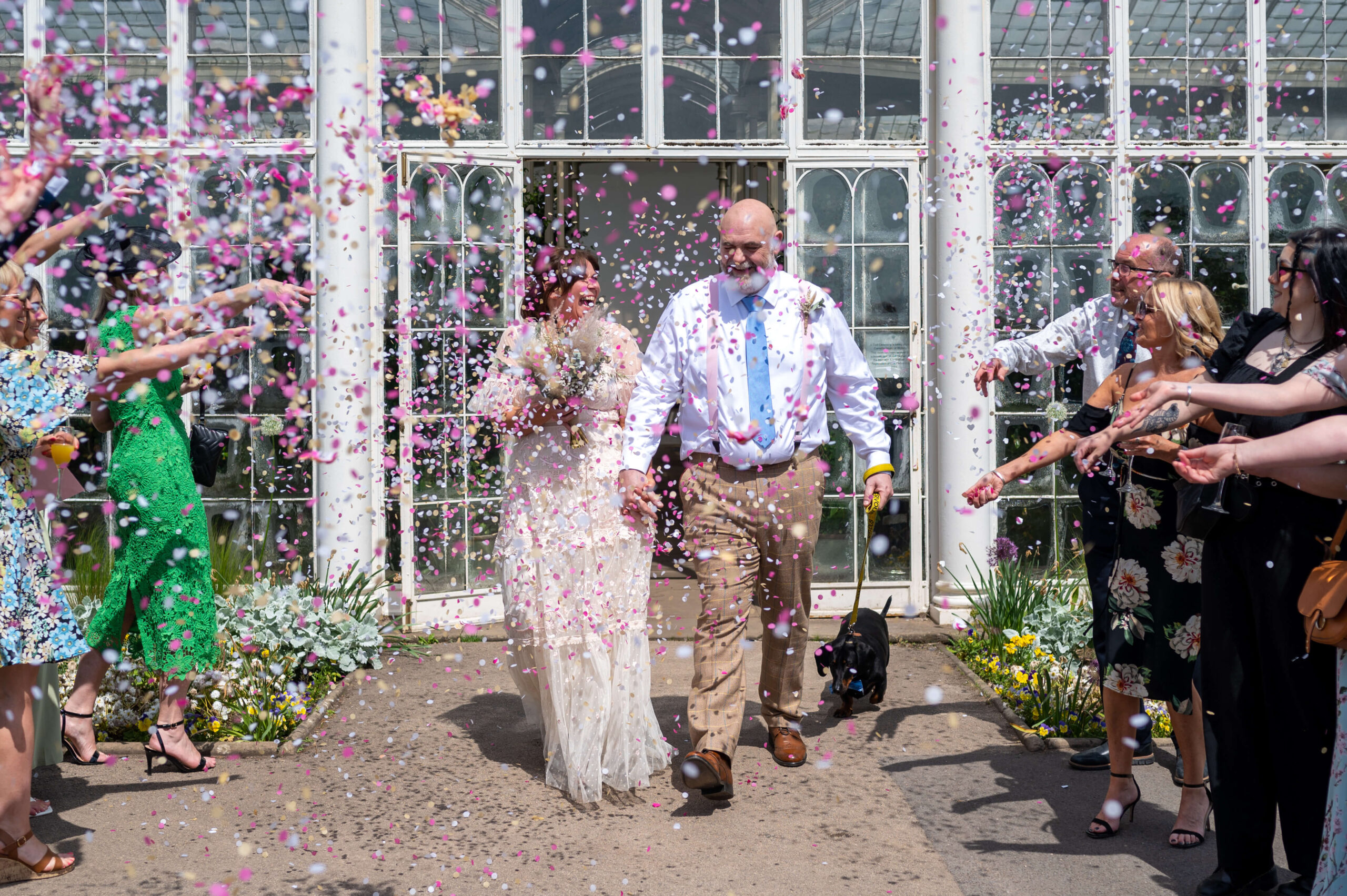 Joyful wedding couple exiting ceremony in vibrant Walled Garden, Wollaton Hall.