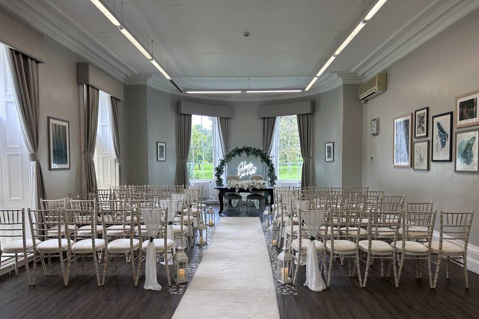 Wedding ceremony setup at Eastwood Hall featuring cross-back chairs and neon focal point.