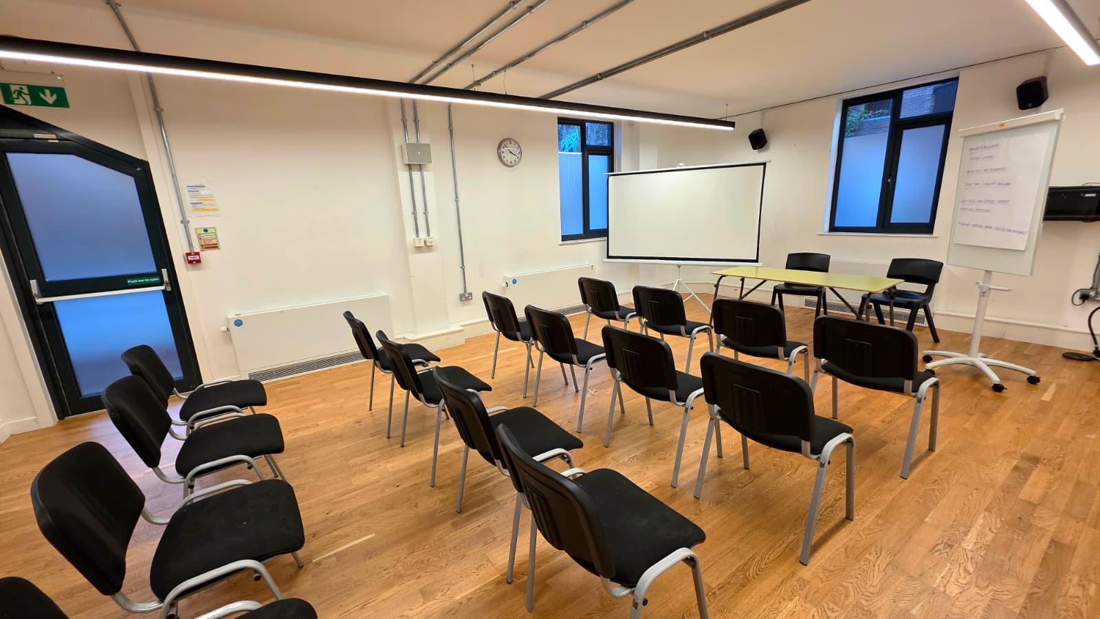 Minimalist meeting room in Chelsea Theatre, featuring black chairs and a whiteboard for workshops.