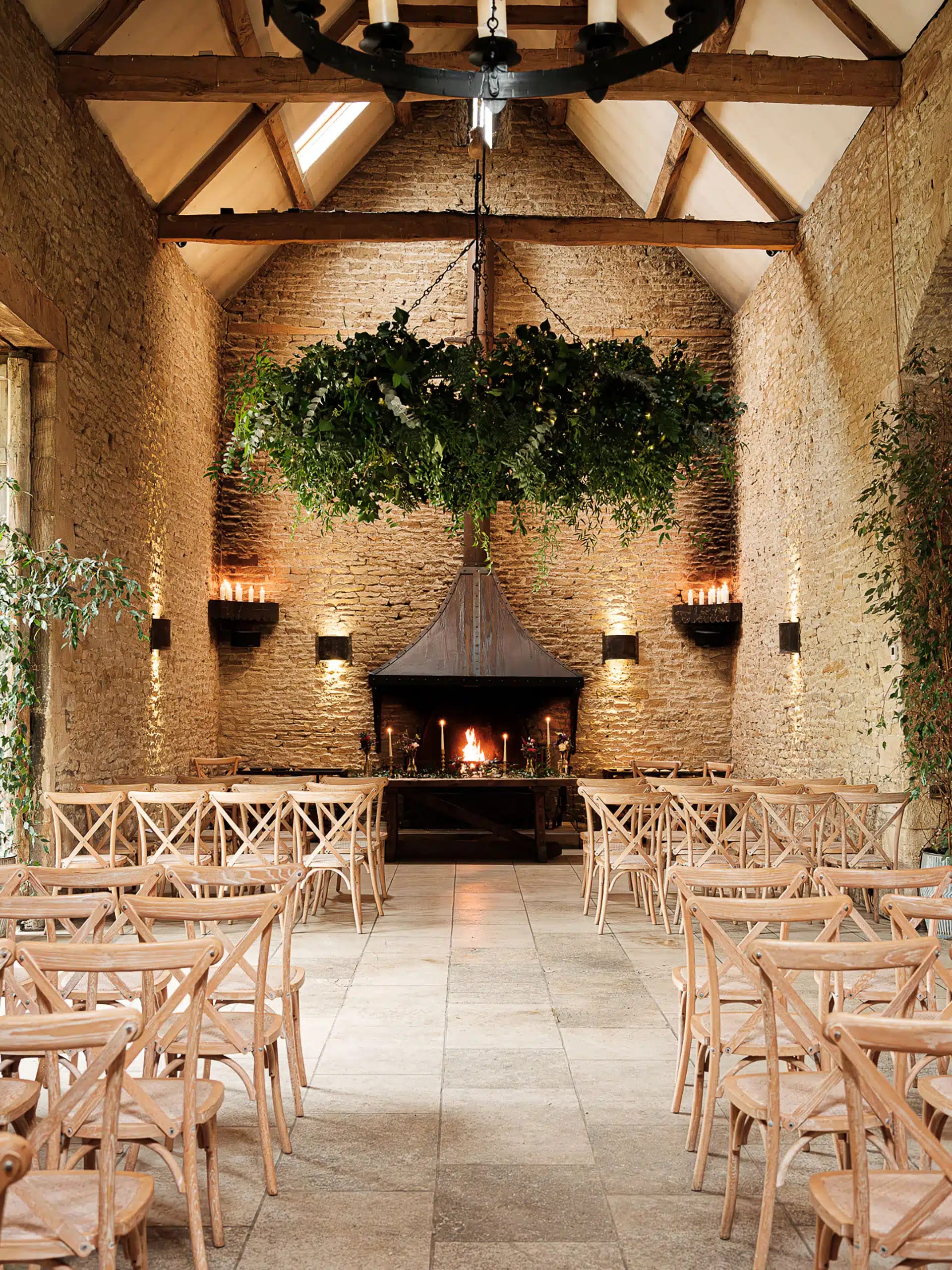 Rustic barn wedding ceremony with botanical chandelier and fireplace for event venue inspiration.