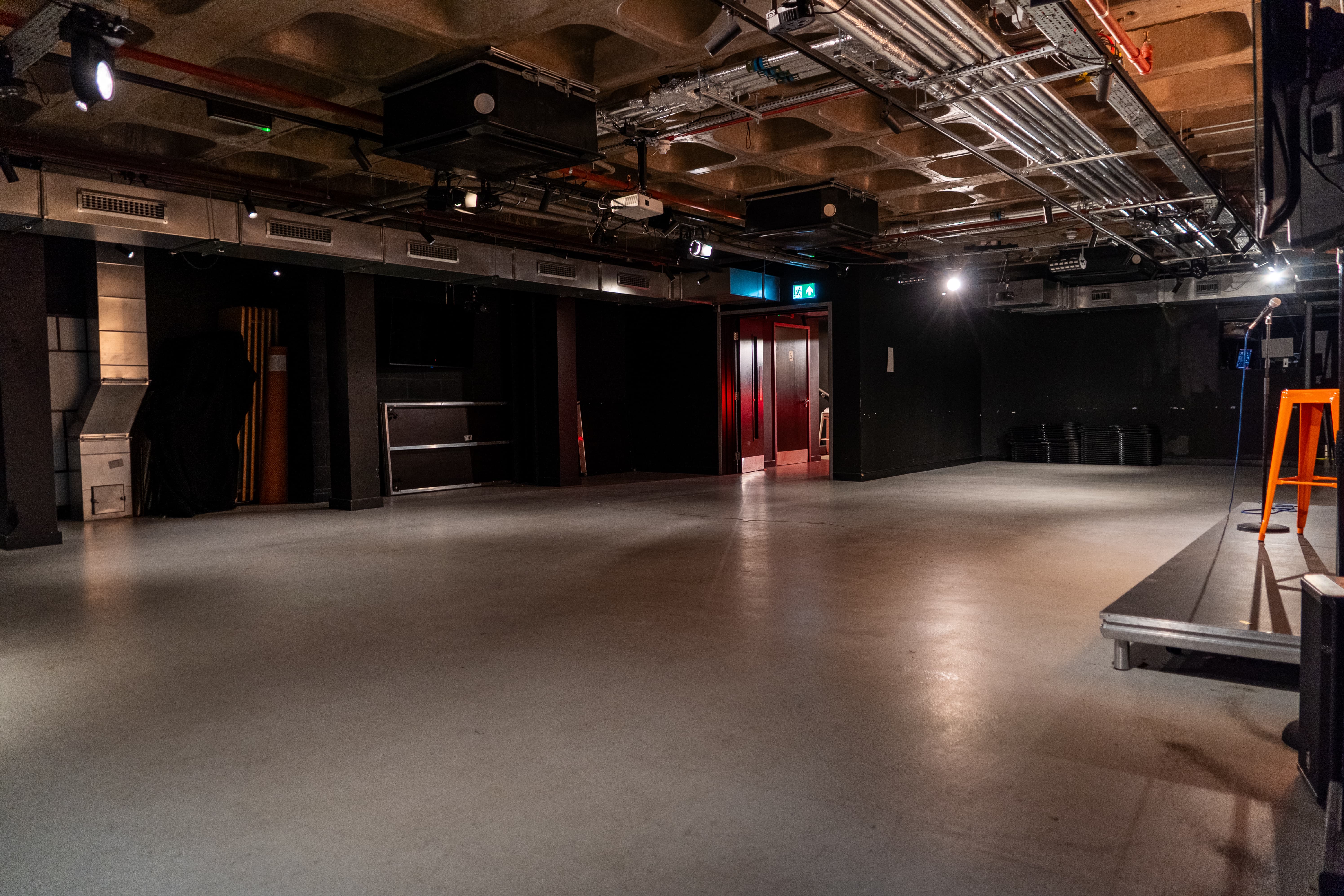 Industrial Big Belly Room event space with stage for corporate workshops and evening receptions.